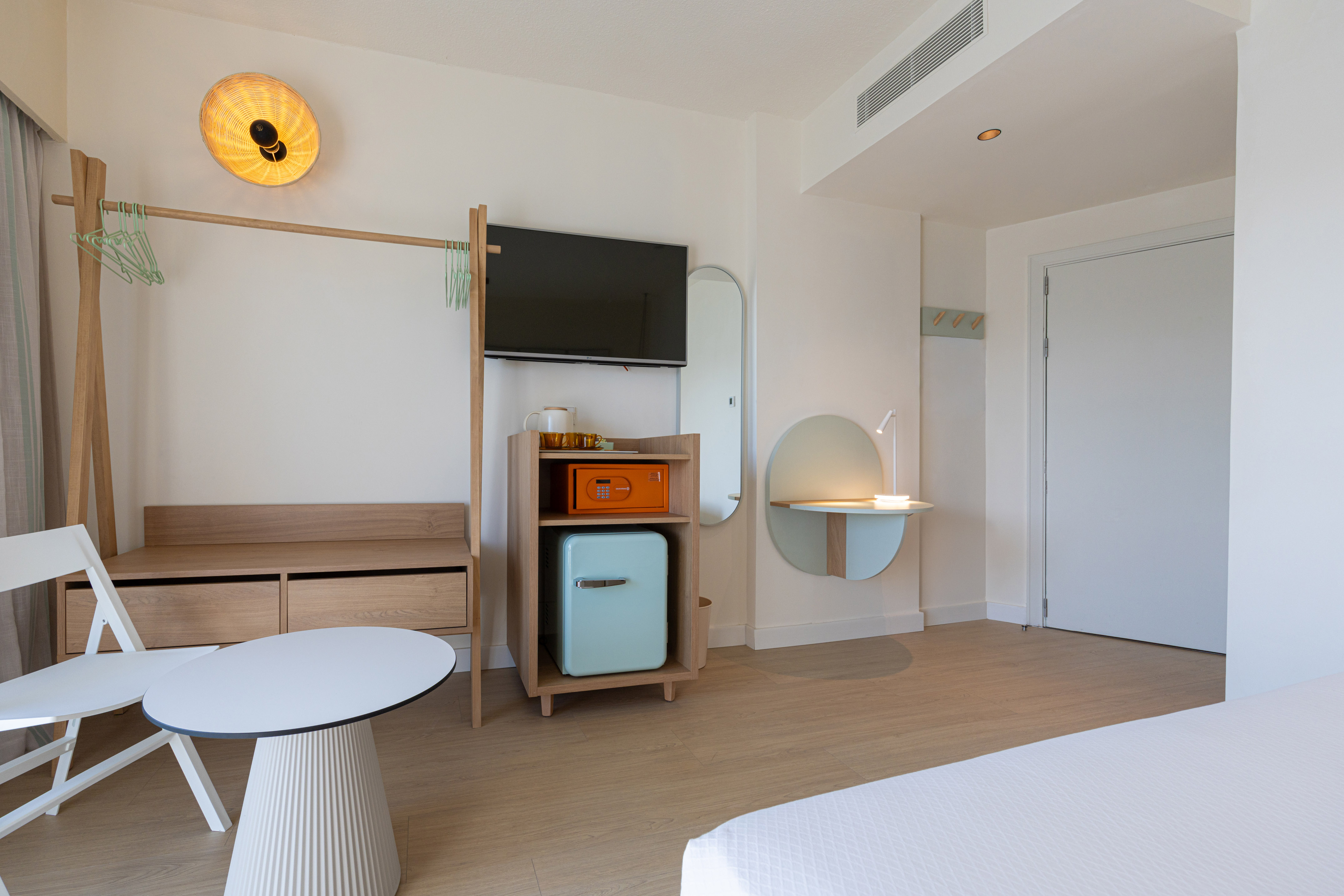 Minimalist hotel room with TV, mini-fridge, wooden furniture, and desk.