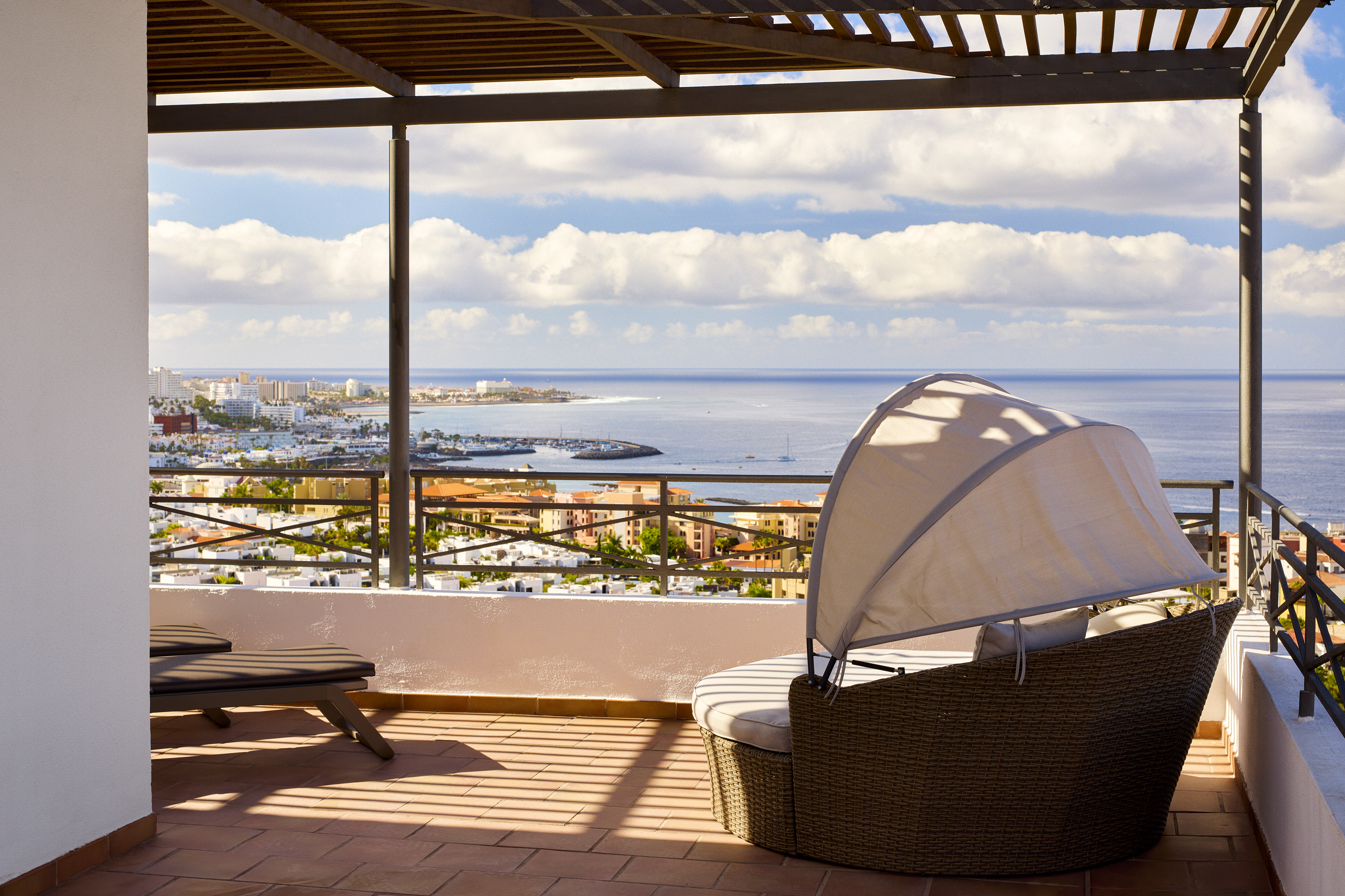 Balcony with panoramic ocean and coastal town view, wicker daybed.