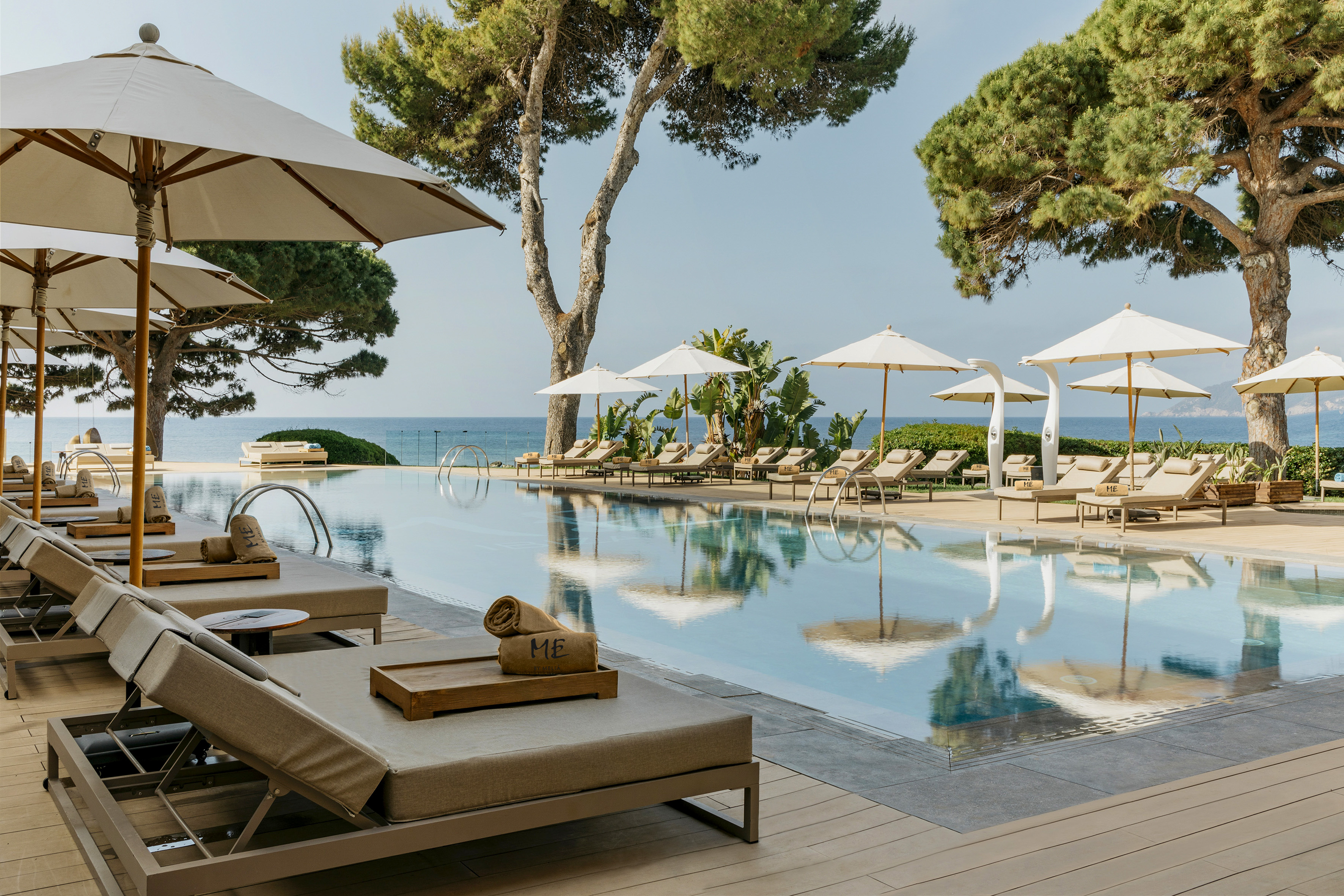 Oceanfront luxury resort infinity pool with sun loungers and large shade trees.