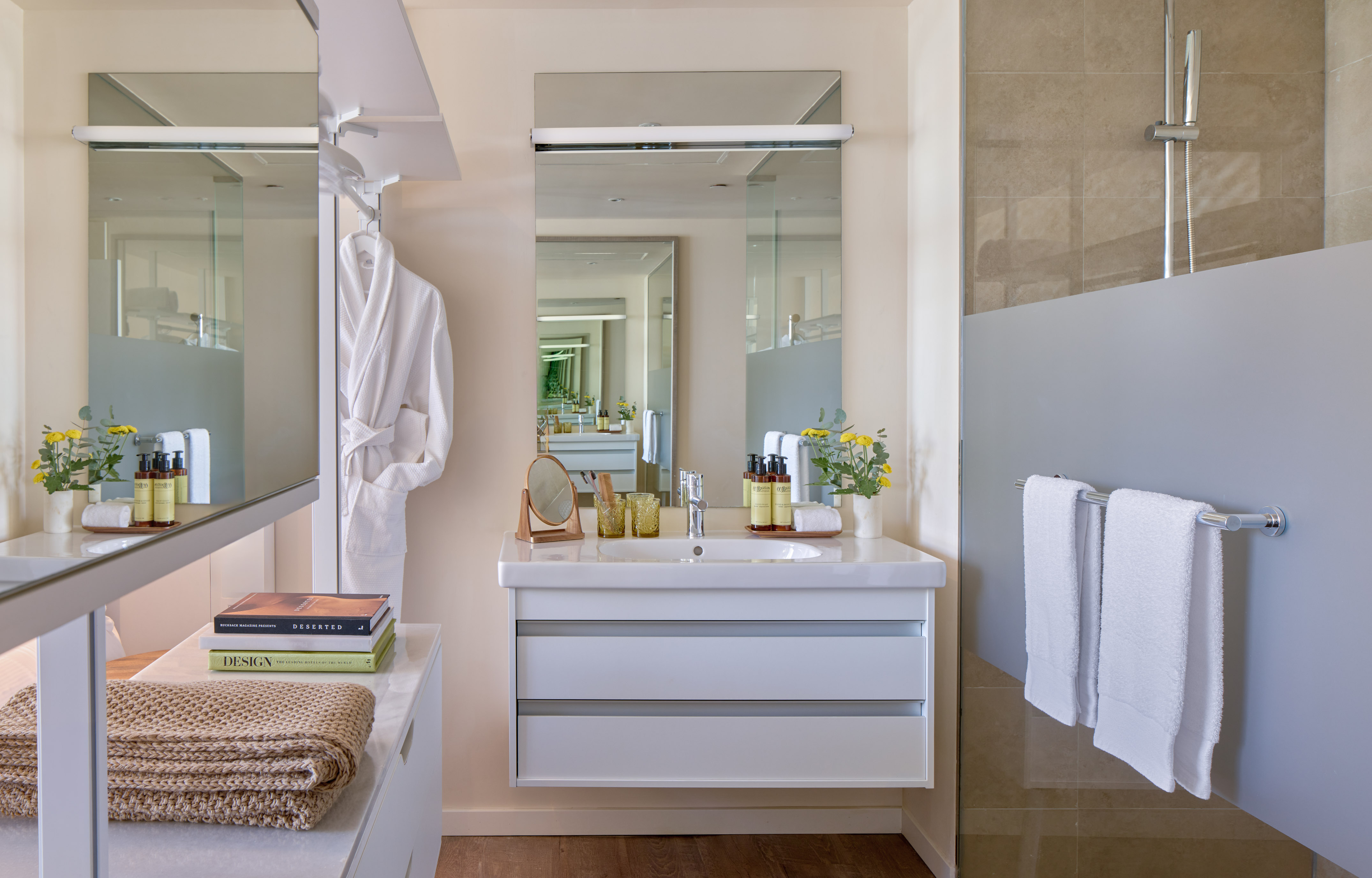 Modern bathroom with white vanity, large mirror, shower, towels, and bathrobe.