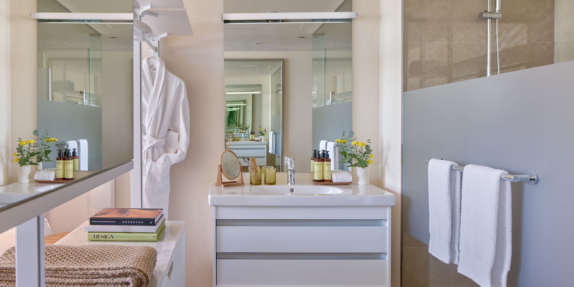 Modern bathroom with white vanity, large mirror, shower, towels, and bathrobe.