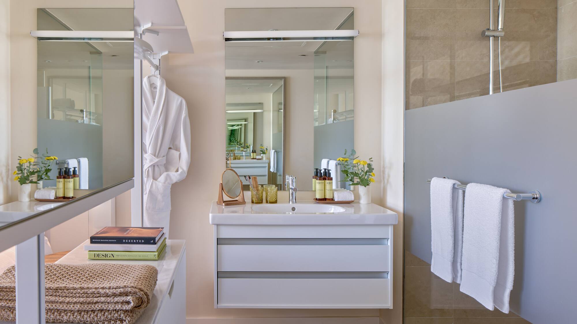 Modern bathroom with white vanity, large mirror, shower, towels, and bathrobe.