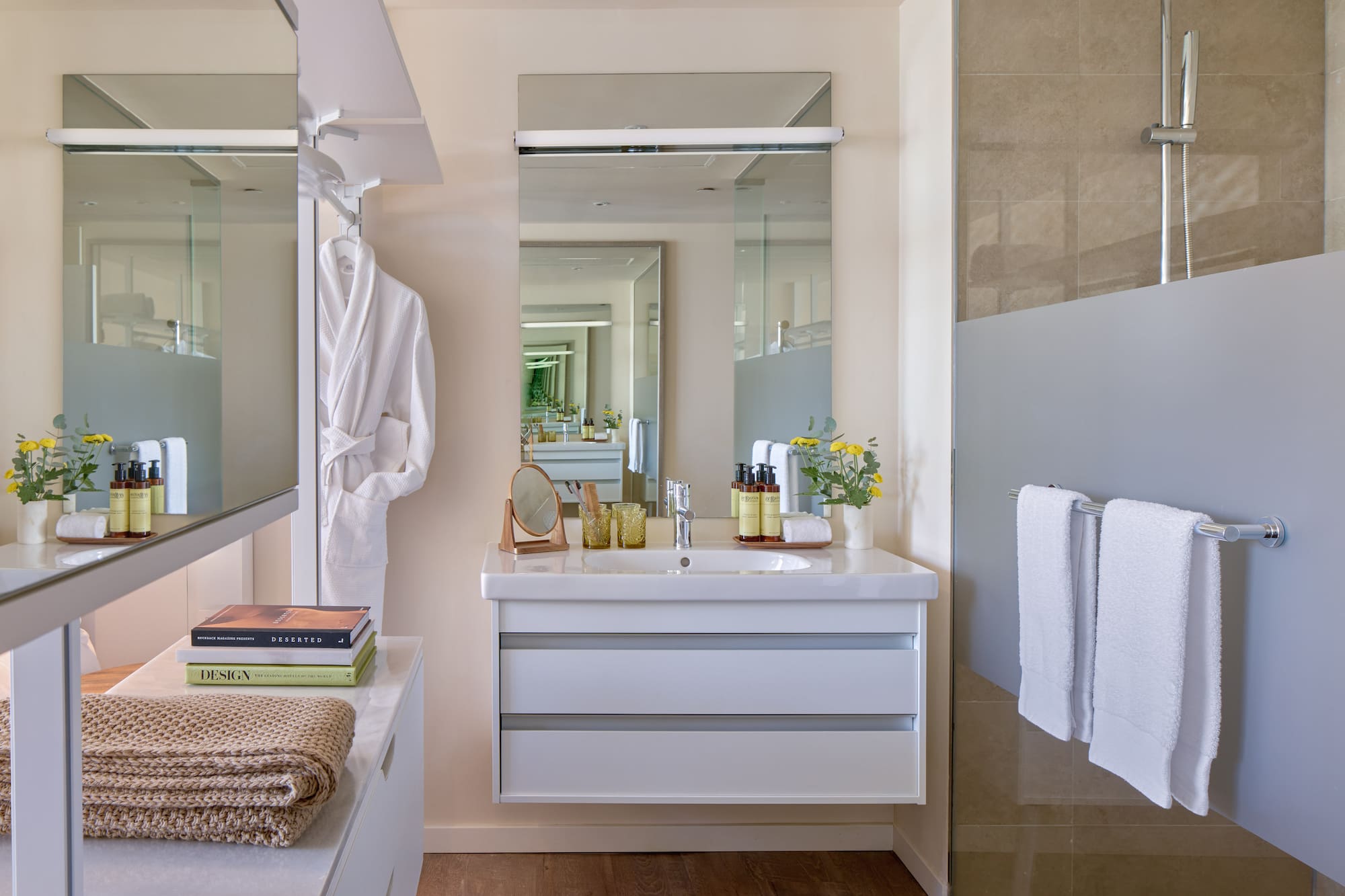 Modern bathroom with white vanity, large mirror, shower, towels, and bathrobe.