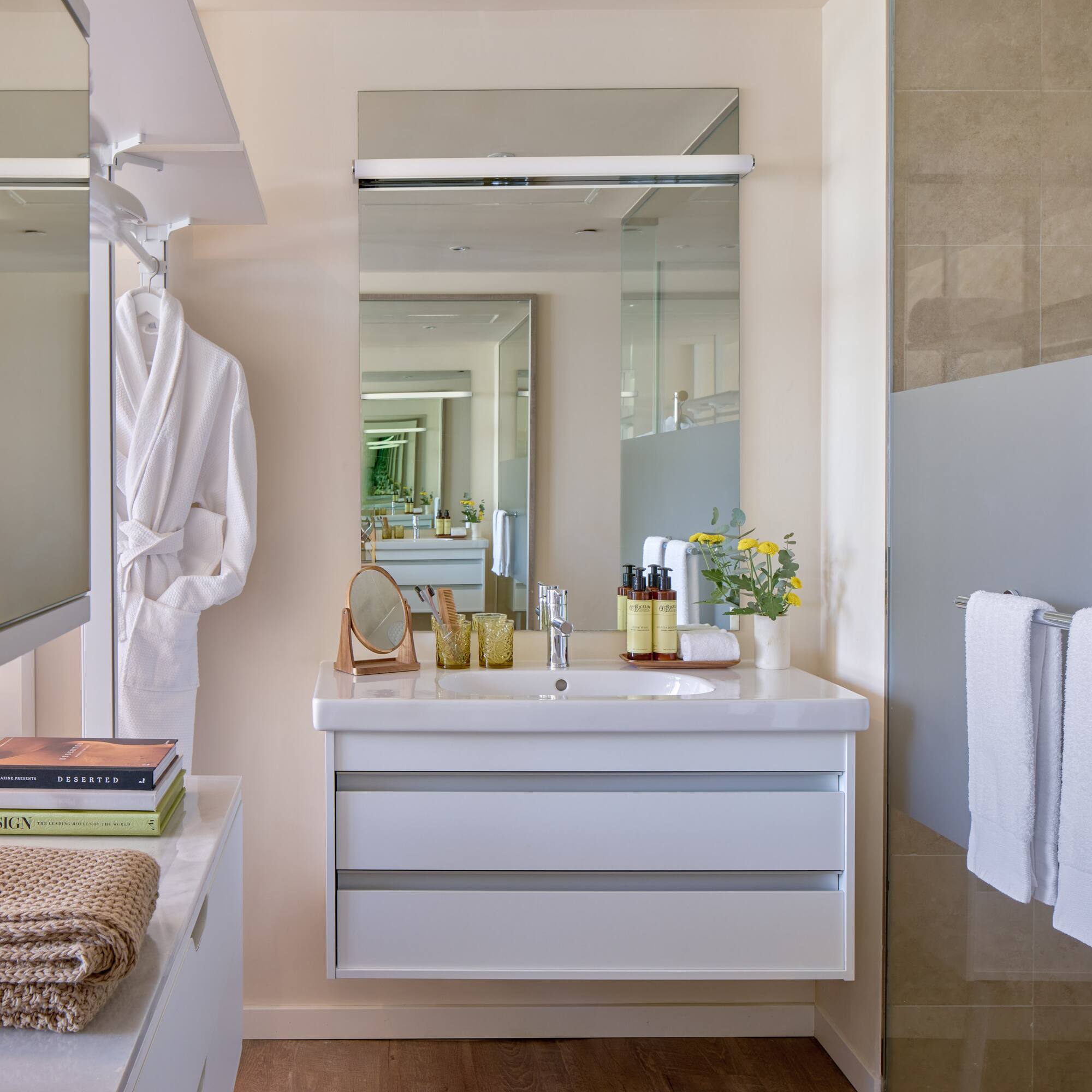 Modern bathroom with white vanity, large mirror, shower, towels, and bathrobe.