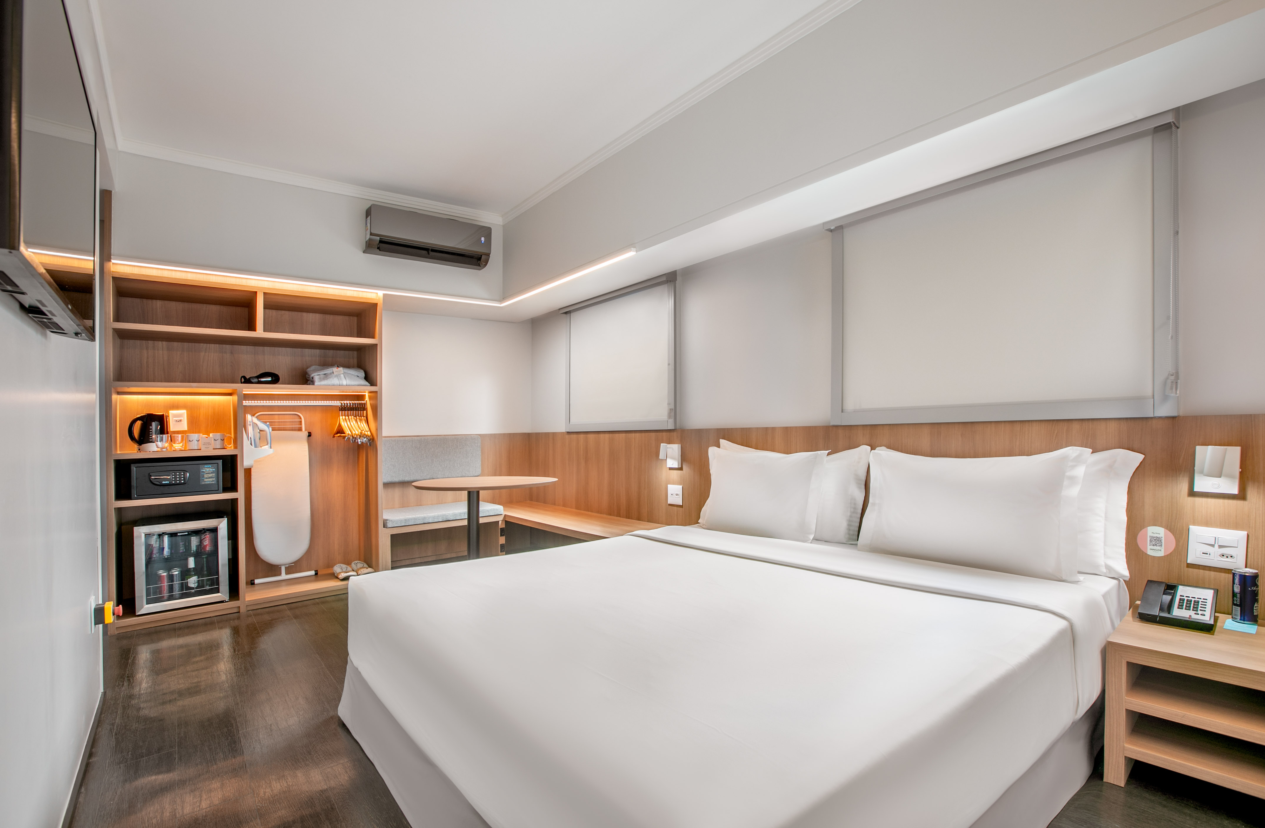 Hotel room with white bed, wooden storage unit, minibar, and light decor.