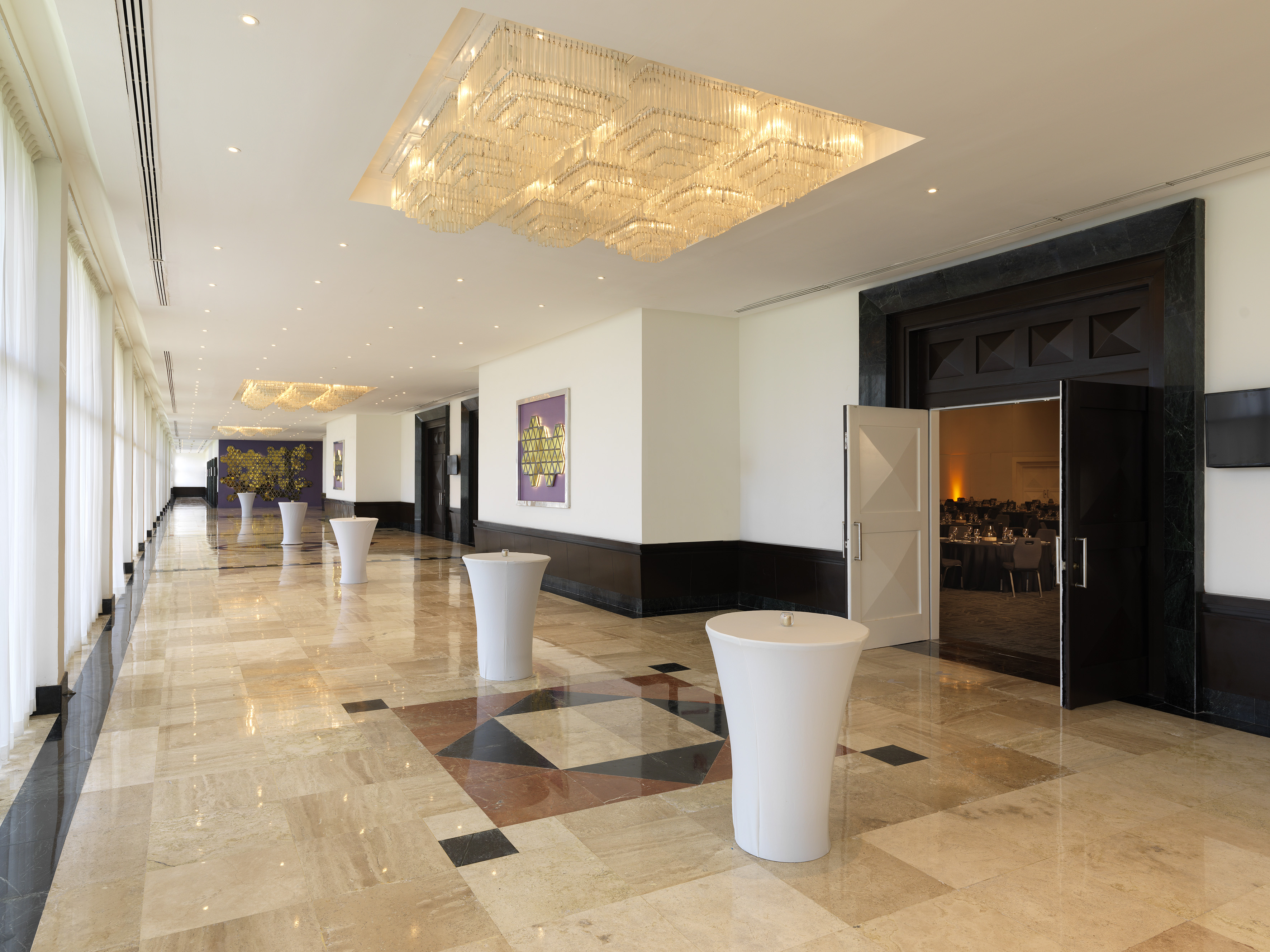 Elegant hotel corridor with marble floor, crystal chandeliers, and open event room.
