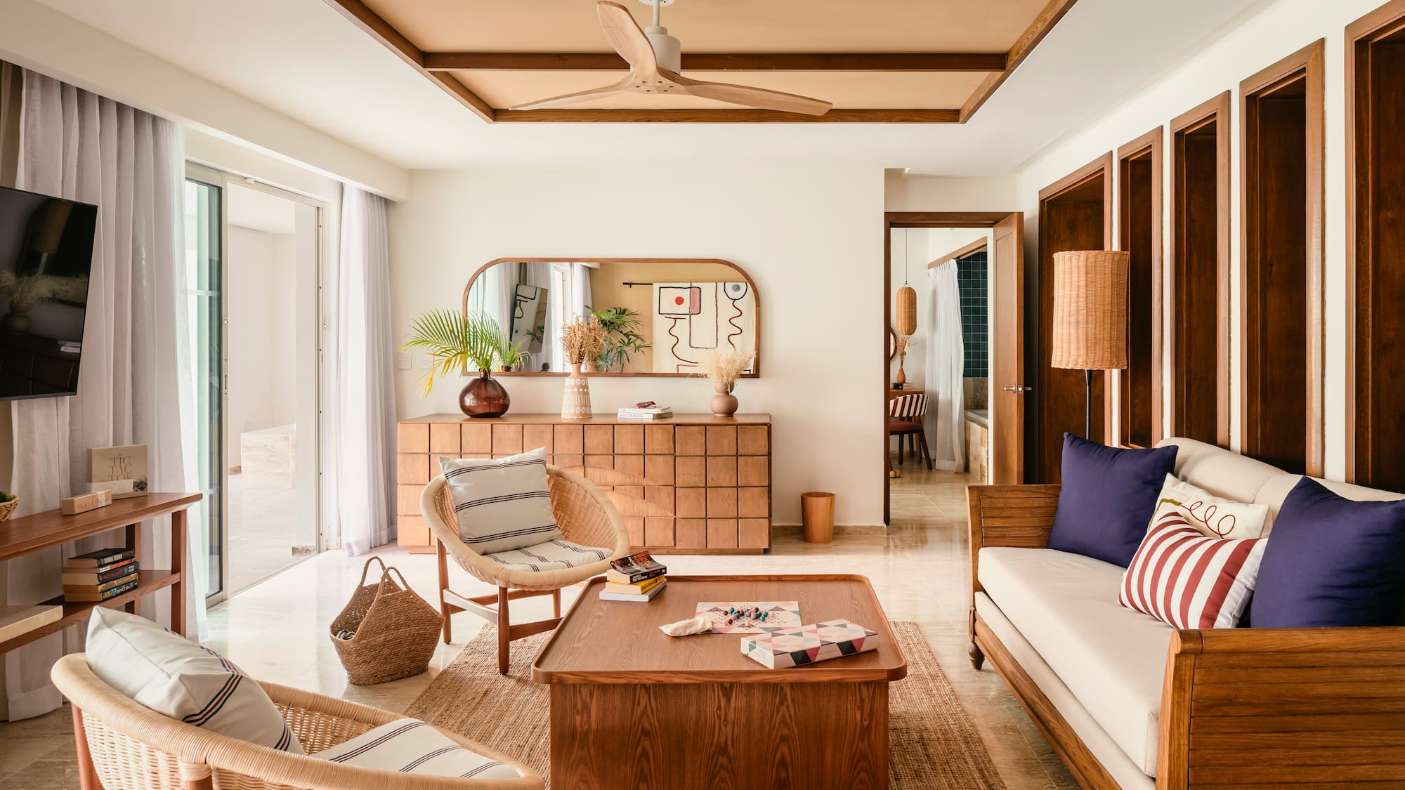 Bright modern living room with wooden furniture, rattan chairs, and tropical plants.