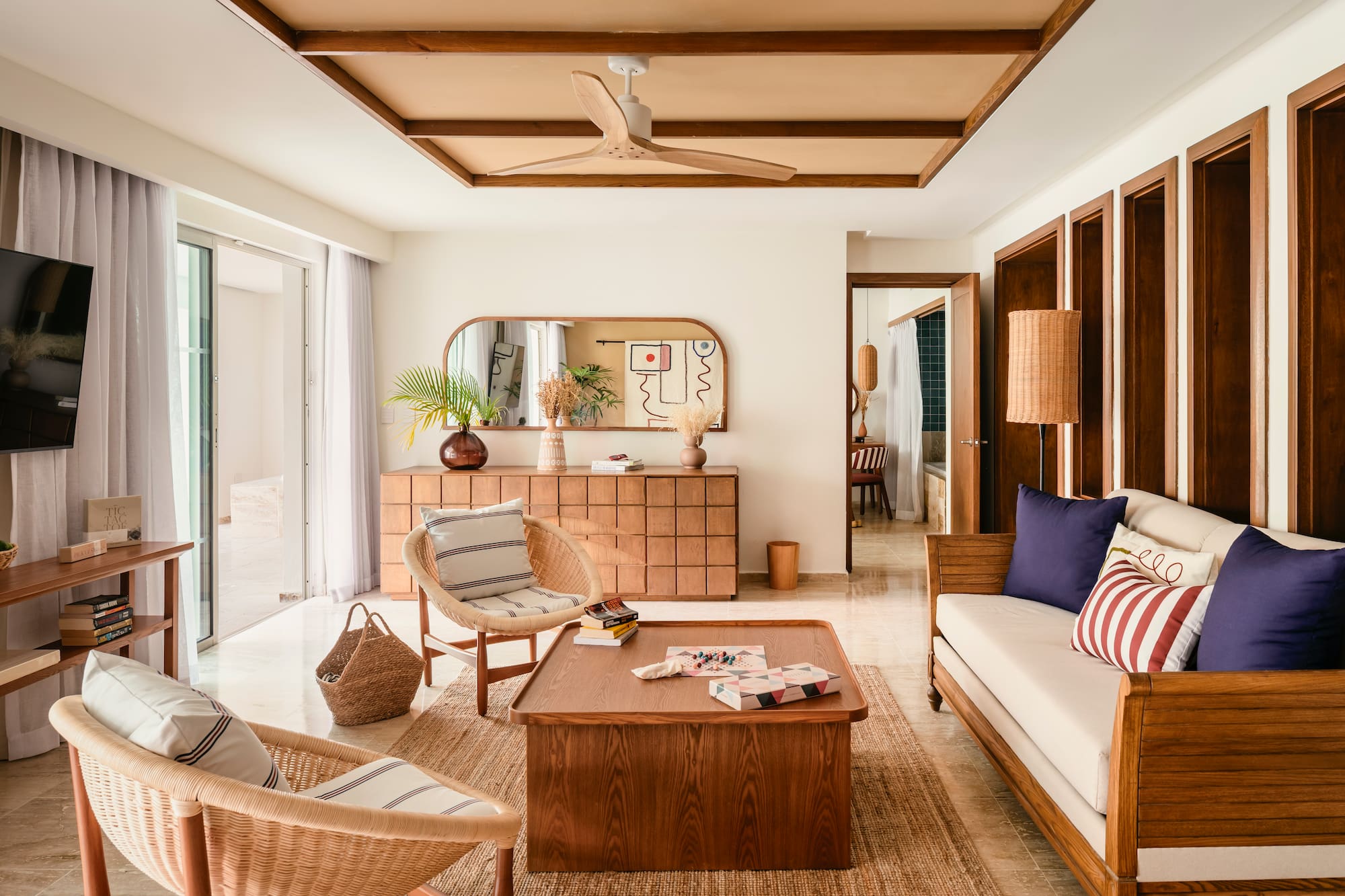 Bright modern living room with wooden furniture, rattan chairs, and tropical plants.