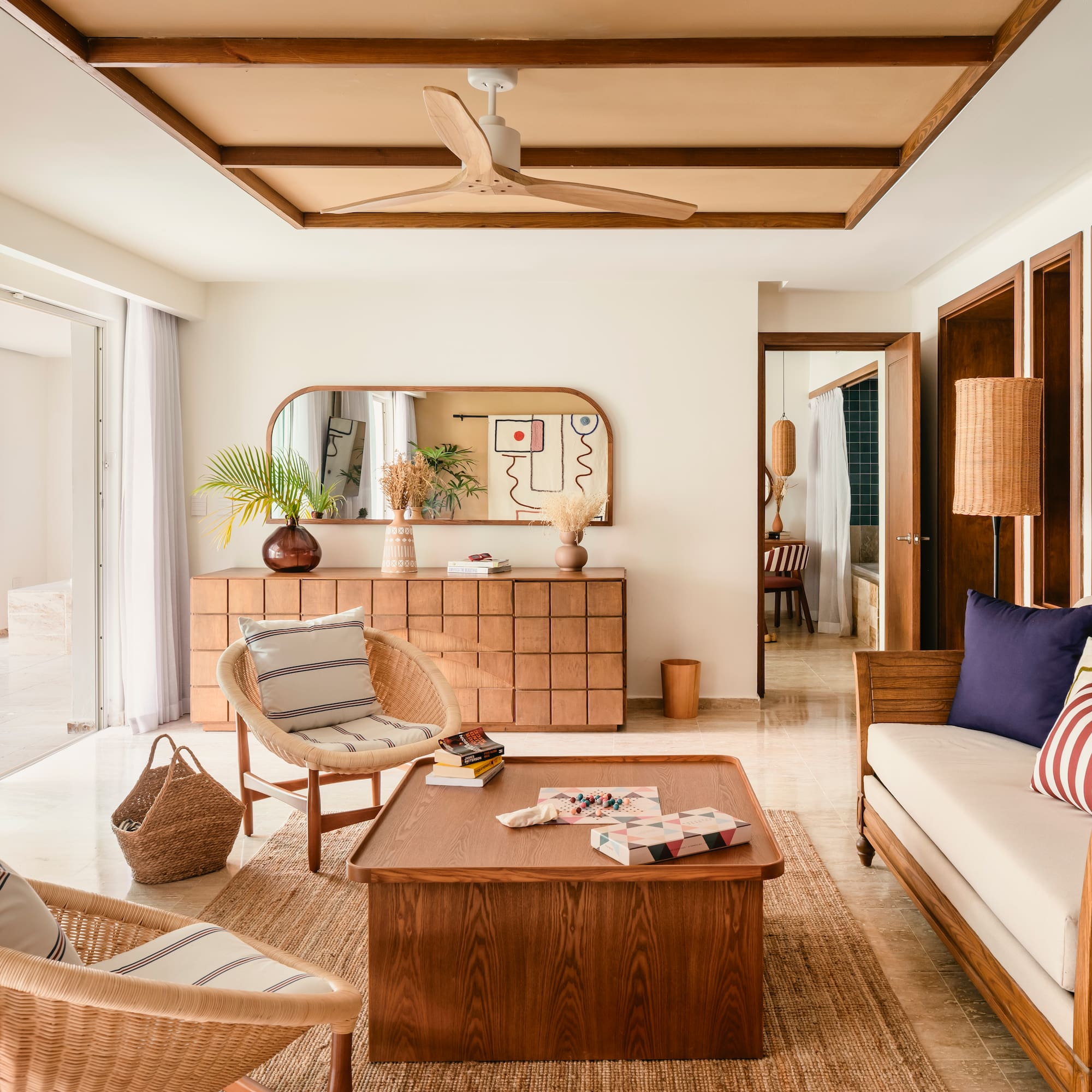 Bright modern living room with wooden furniture, rattan chairs, and tropical plants.
