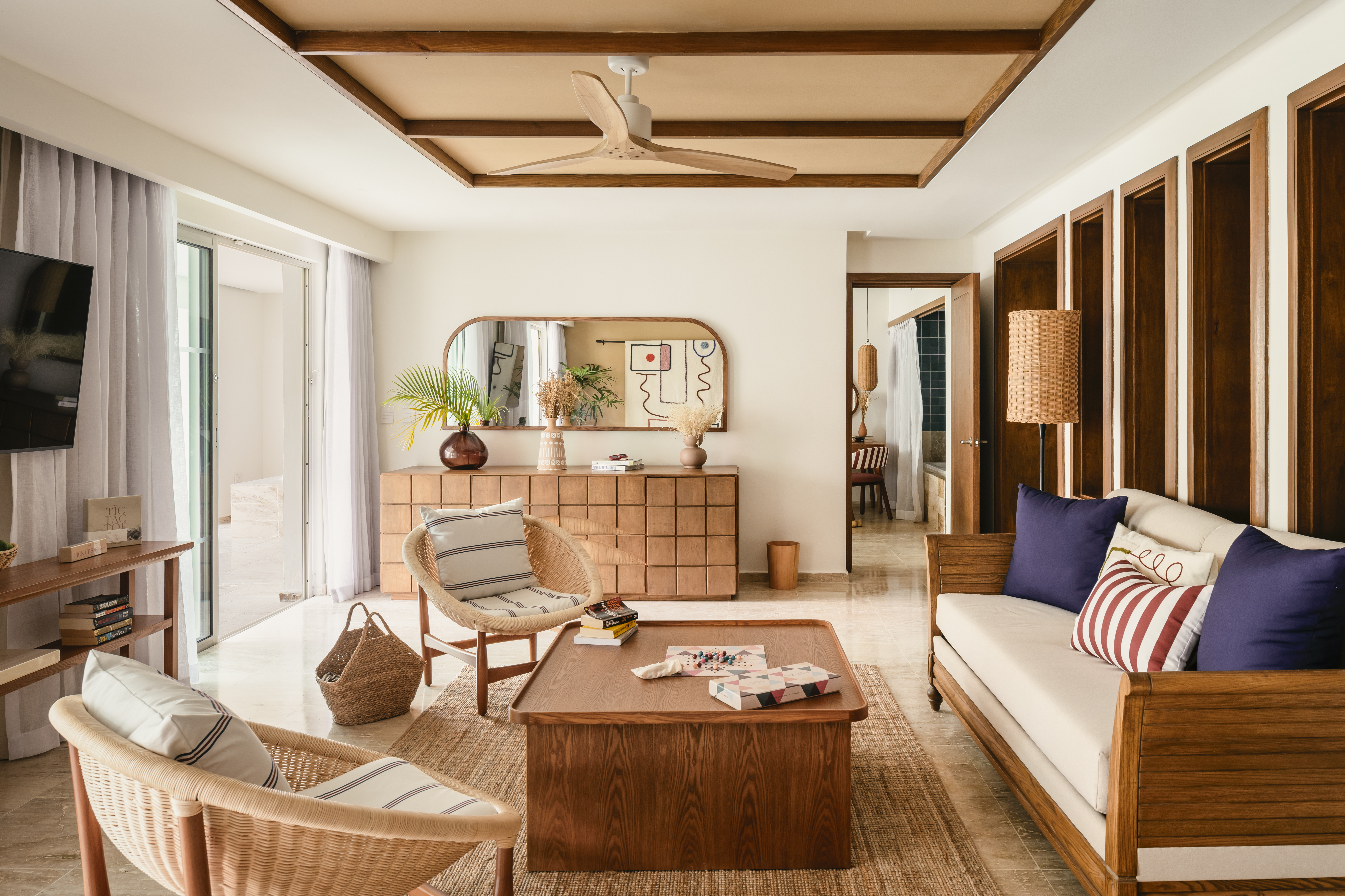 Bright modern living room with wooden furniture, rattan chairs, and tropical plants.
