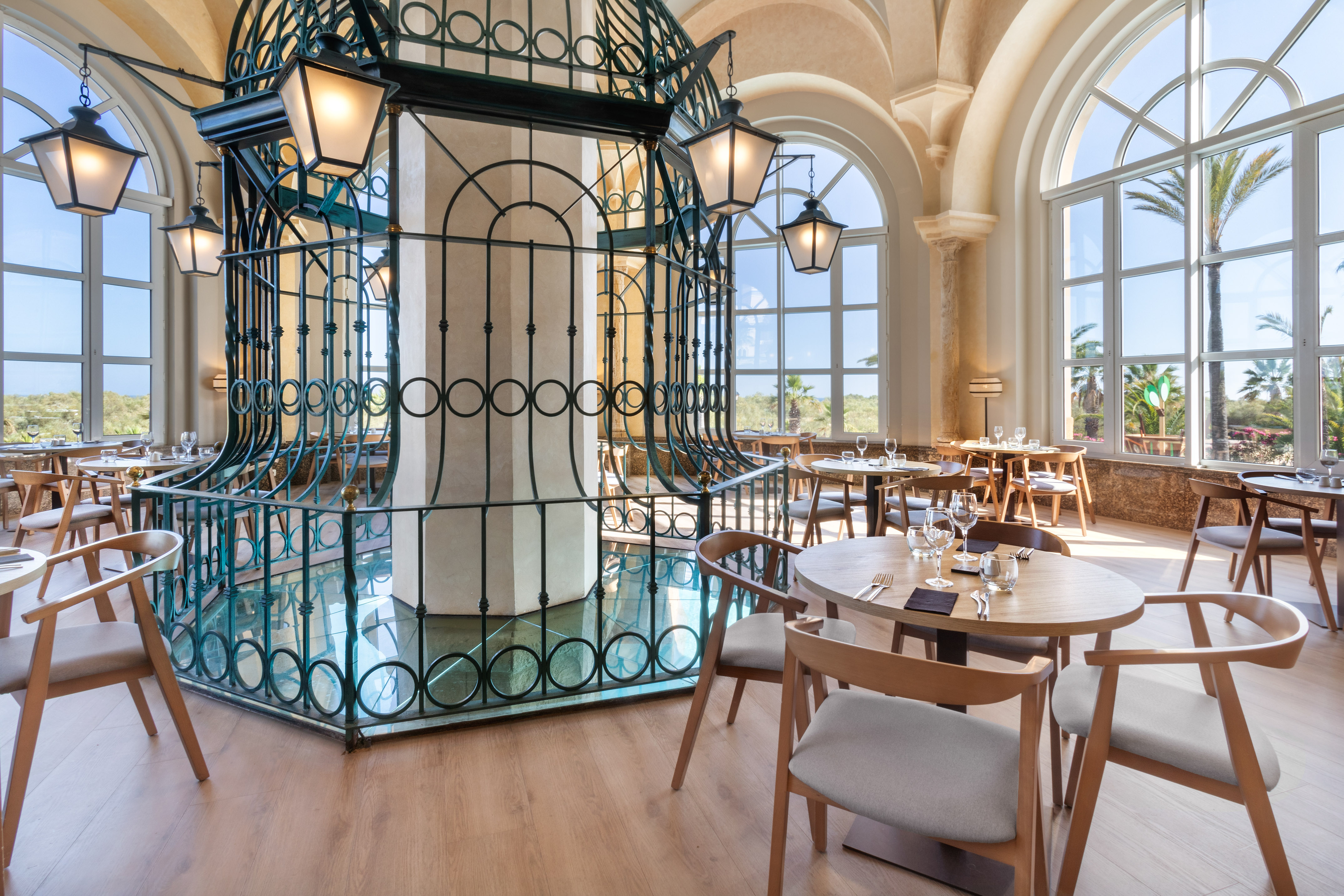 Elegant restaurant interior with arched windows, ornate metalwork, and set tables.