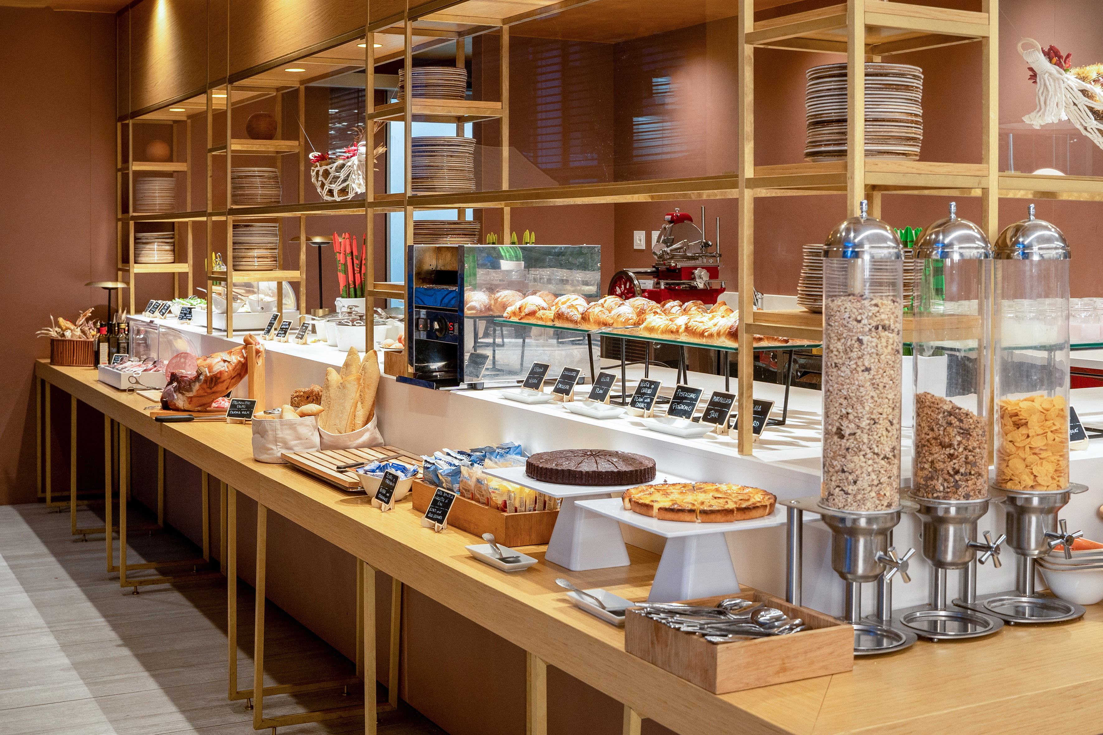 Modern breakfast buffet with pastries, cereals, cured meats, and cakes.