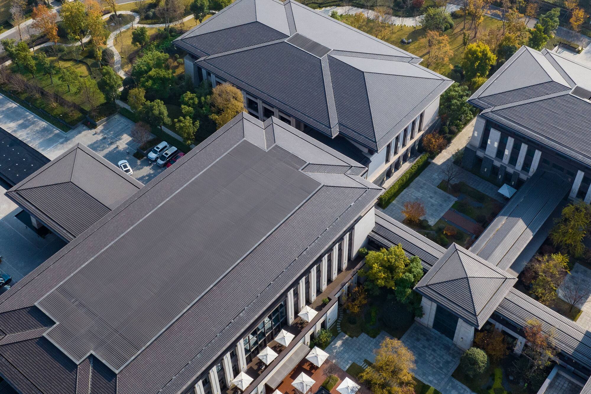 Aerial view of modern buildings with dark roofs, landscaped gardens, autumn trees by a lake.