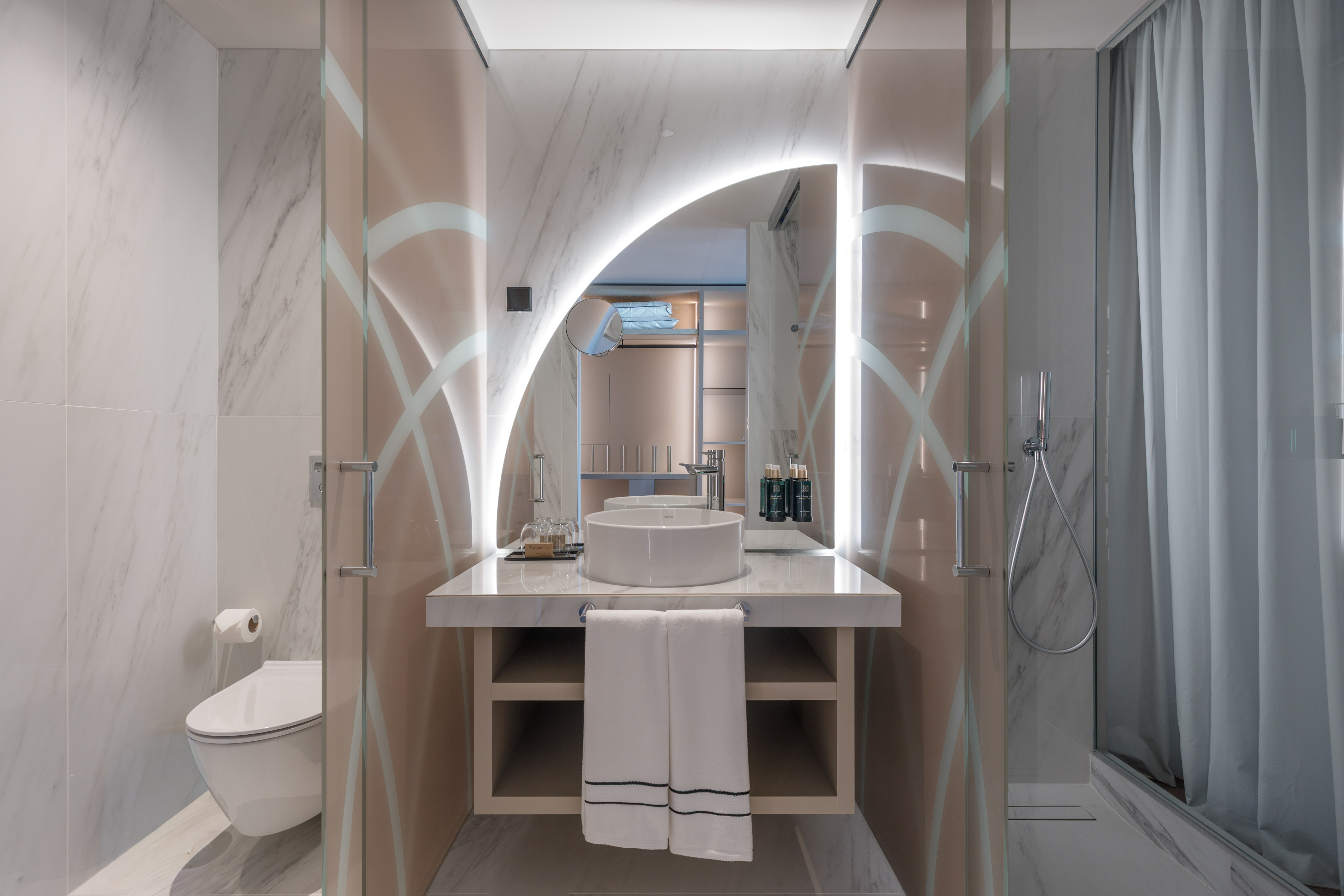 Modern hotel bathroom with illuminated mirror, marble vanity, and vessel sink.