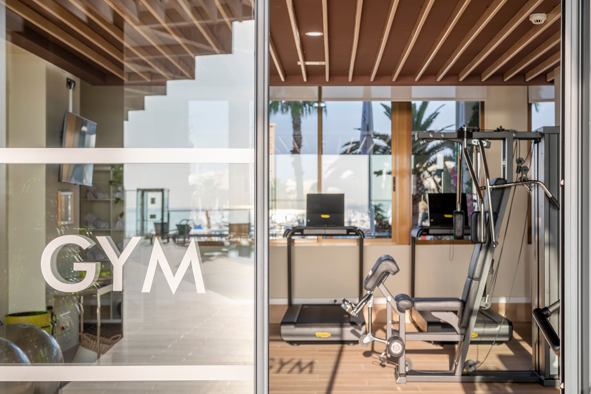 GYM on glass door of modern fitness center with treadmill and weight machine.