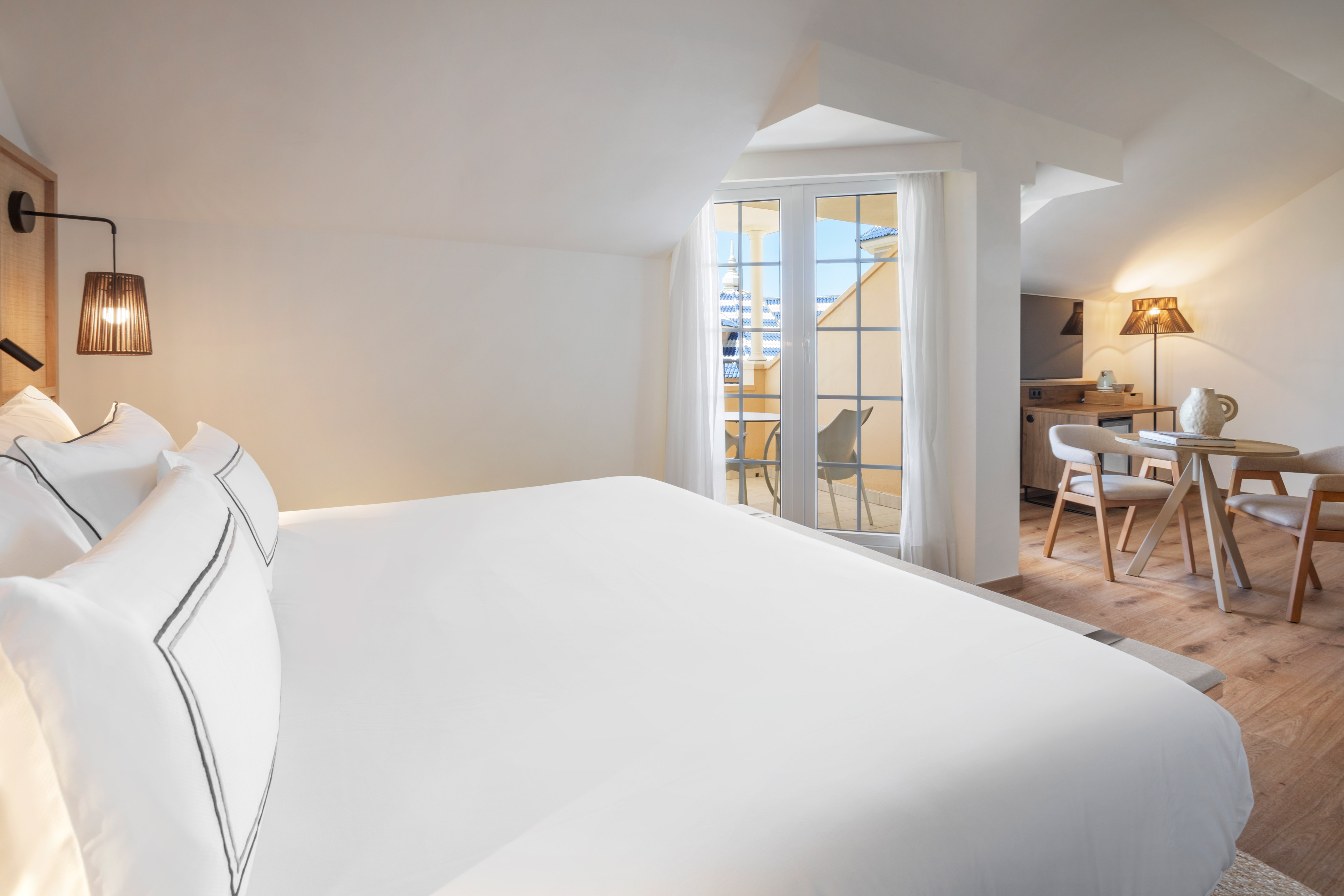 Modern hotel bedroom with white bed, balcony, and light wood furniture.