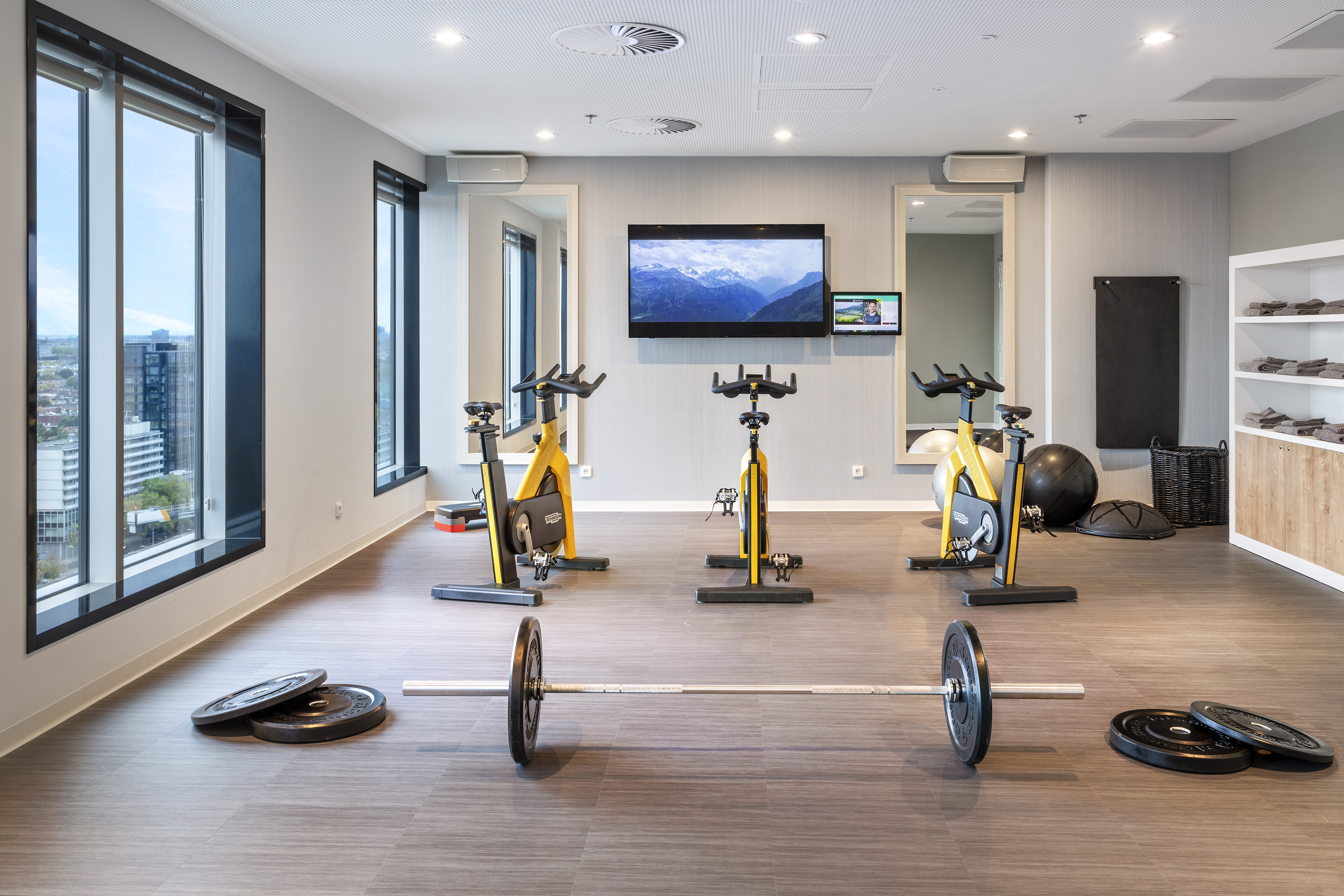 Modern hotel gym with stationary bikes, weights, and city views.