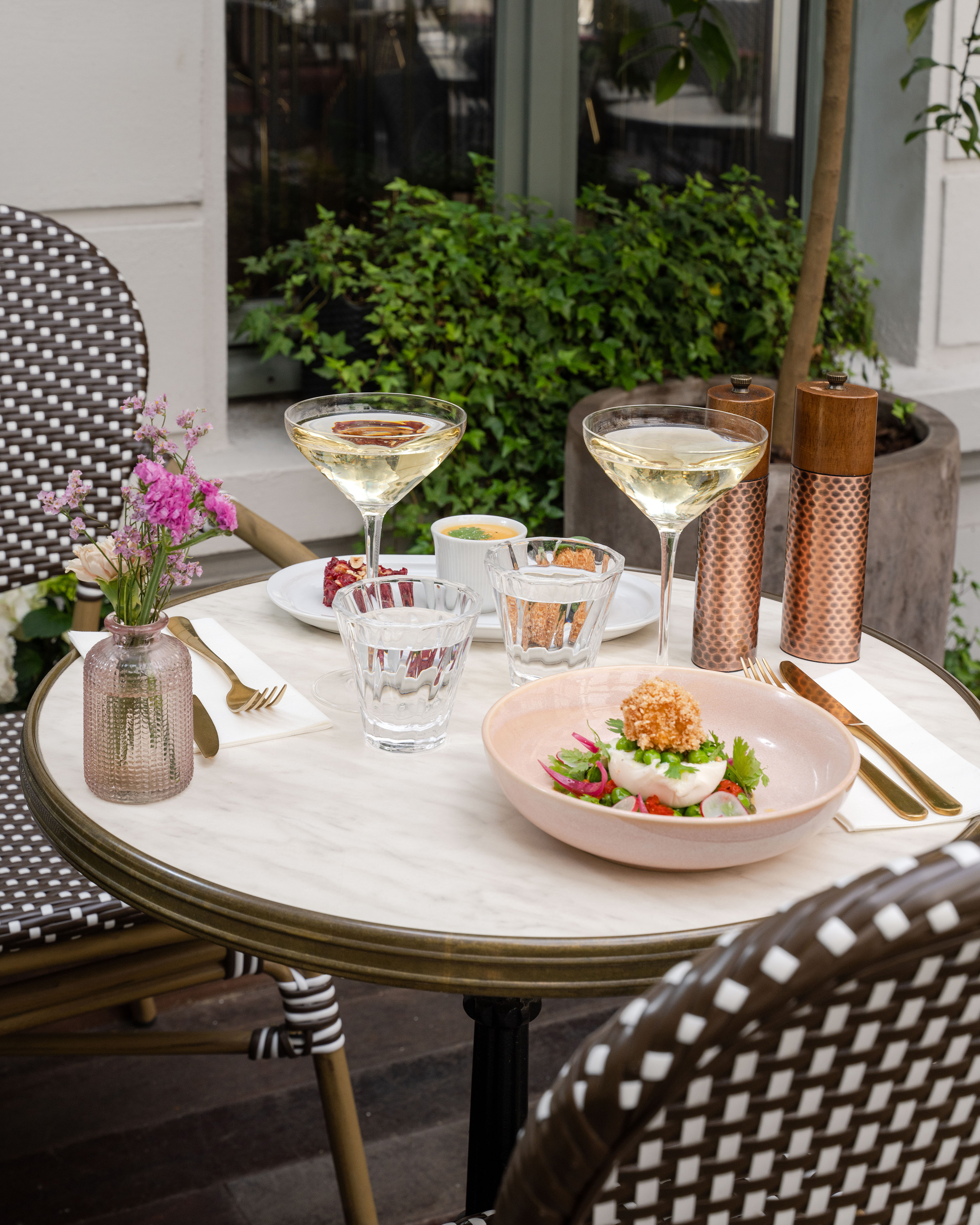 Outdoor bistro table with gourmet dishes, cocktails, and flowers.