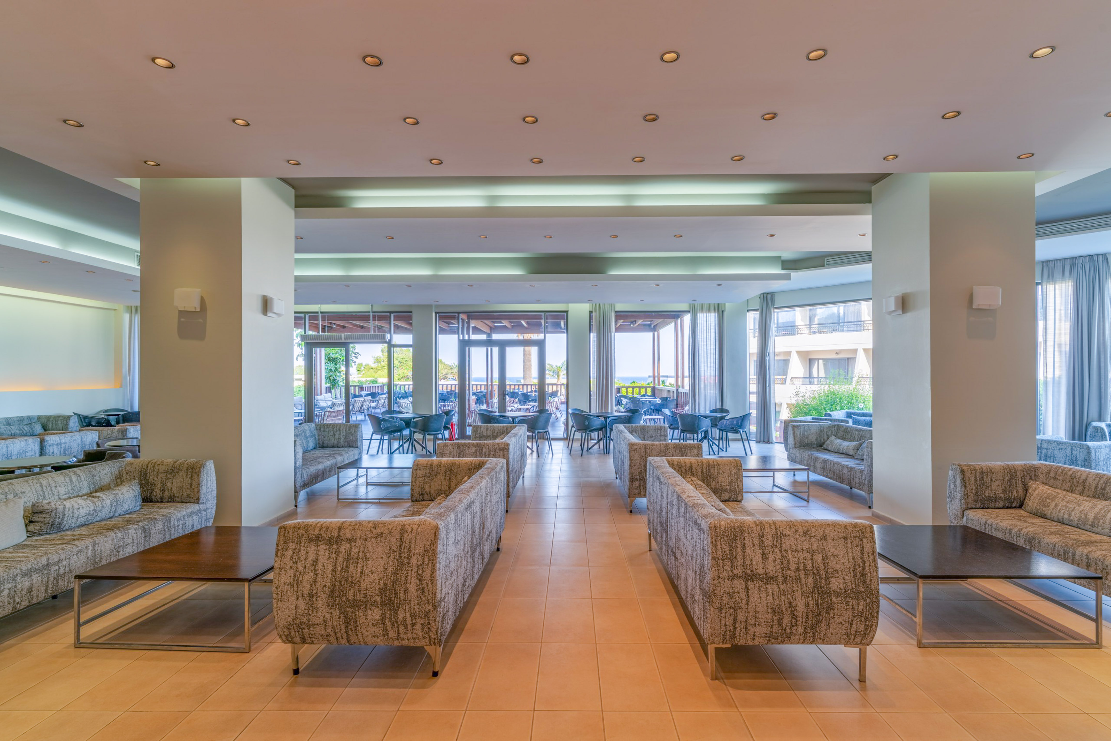 Hotel lounge with modern sofas, tables, and bright view of outdoor patio.