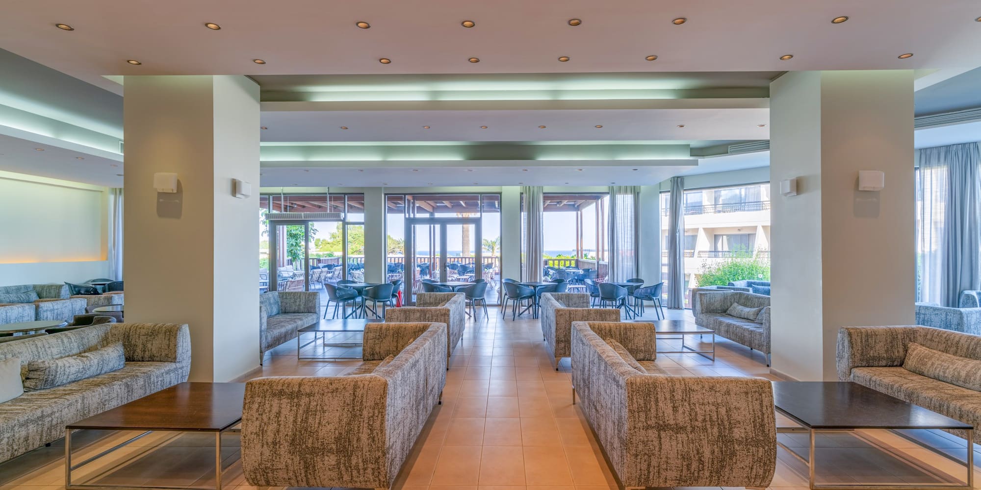 Hotel lounge with modern sofas, tables, and bright view of outdoor patio.