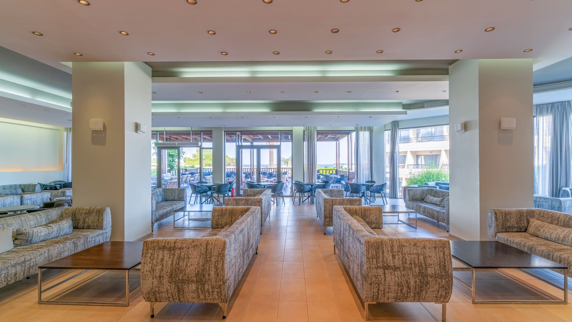 Hotel lounge with modern sofas, tables, and bright view of outdoor patio.