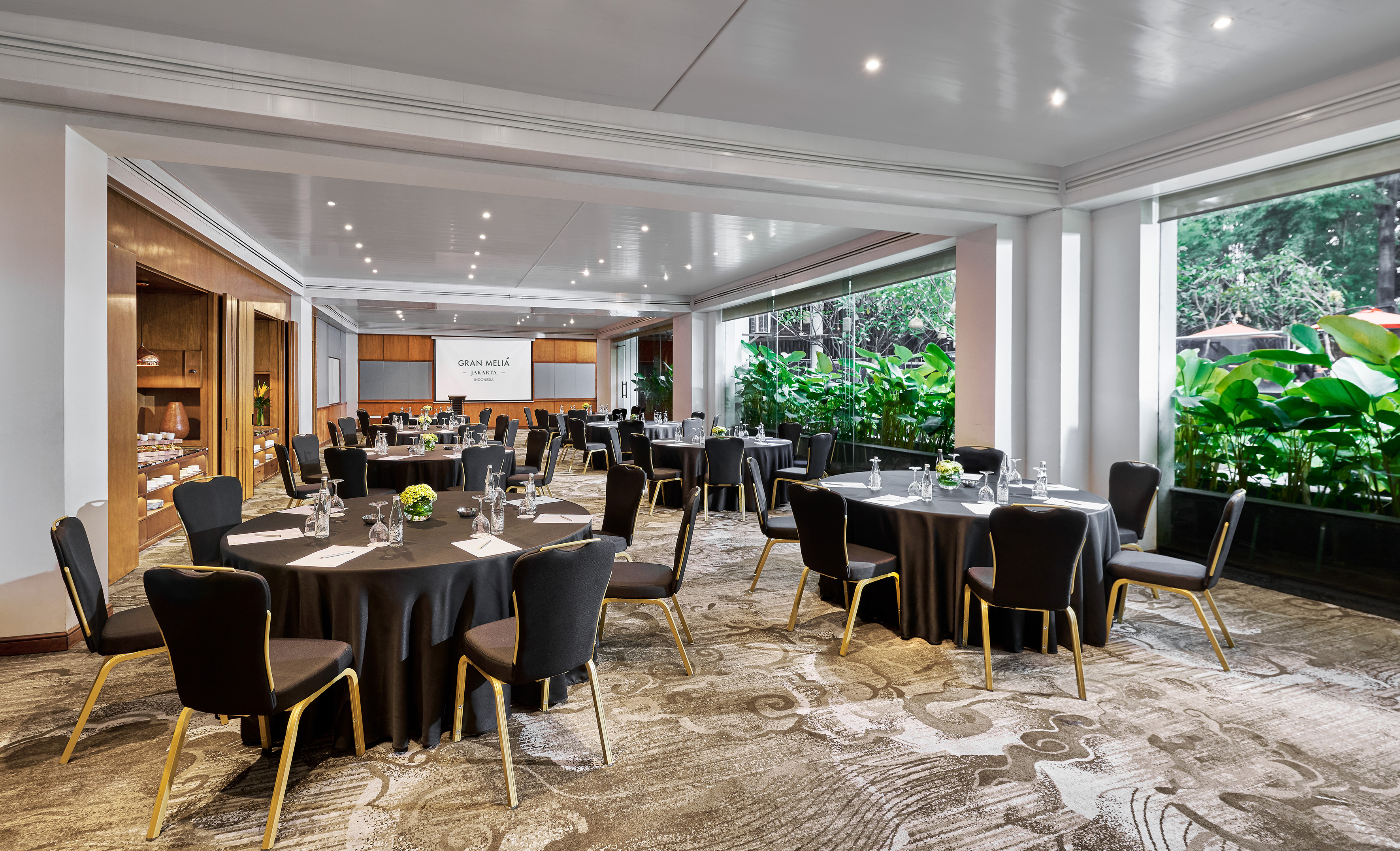 Gran Melia Jakarta meeting room with round tables, screen, and garden view.