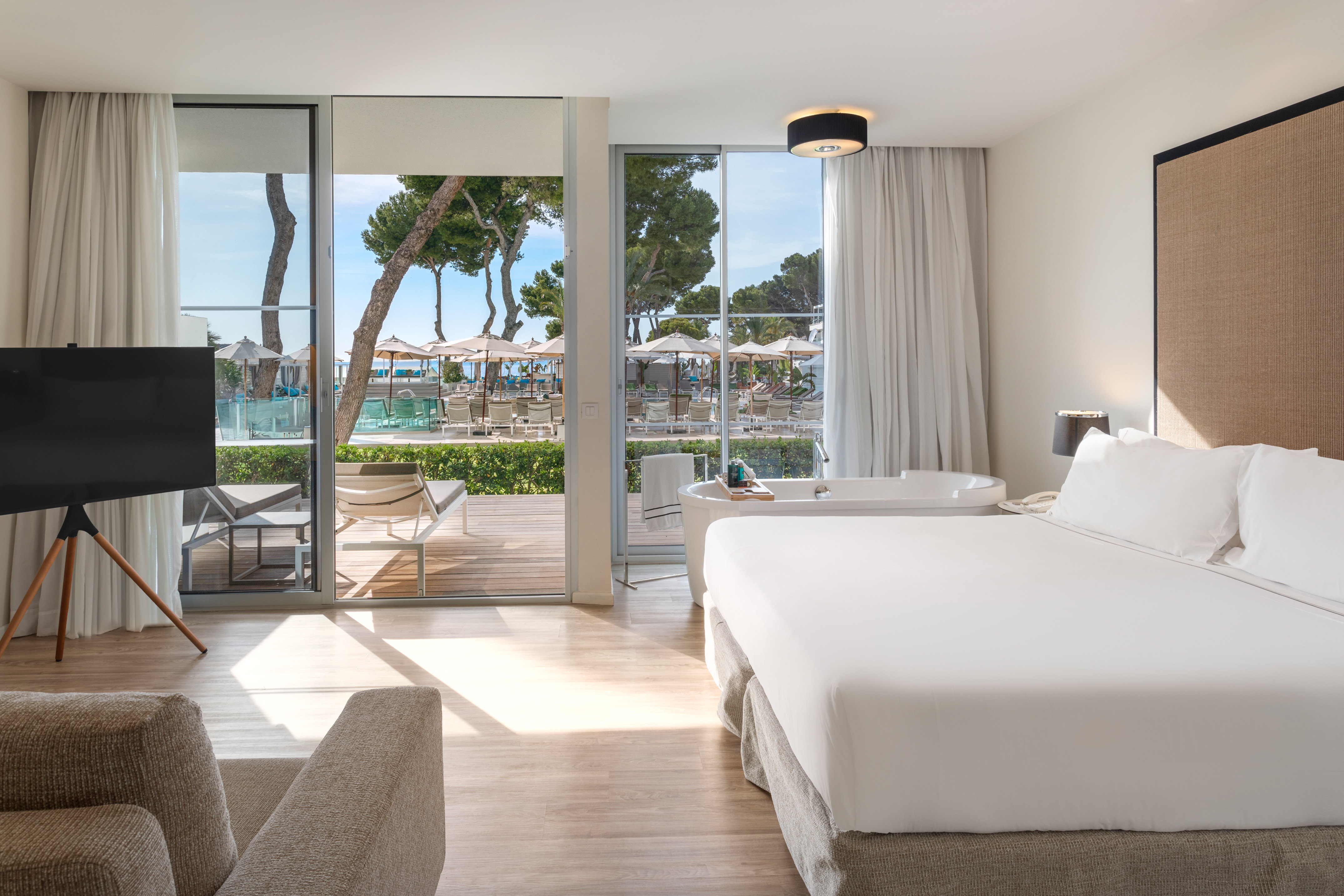 Modern hotel room with bed, bathtub, and sliding doors to resort pool view.