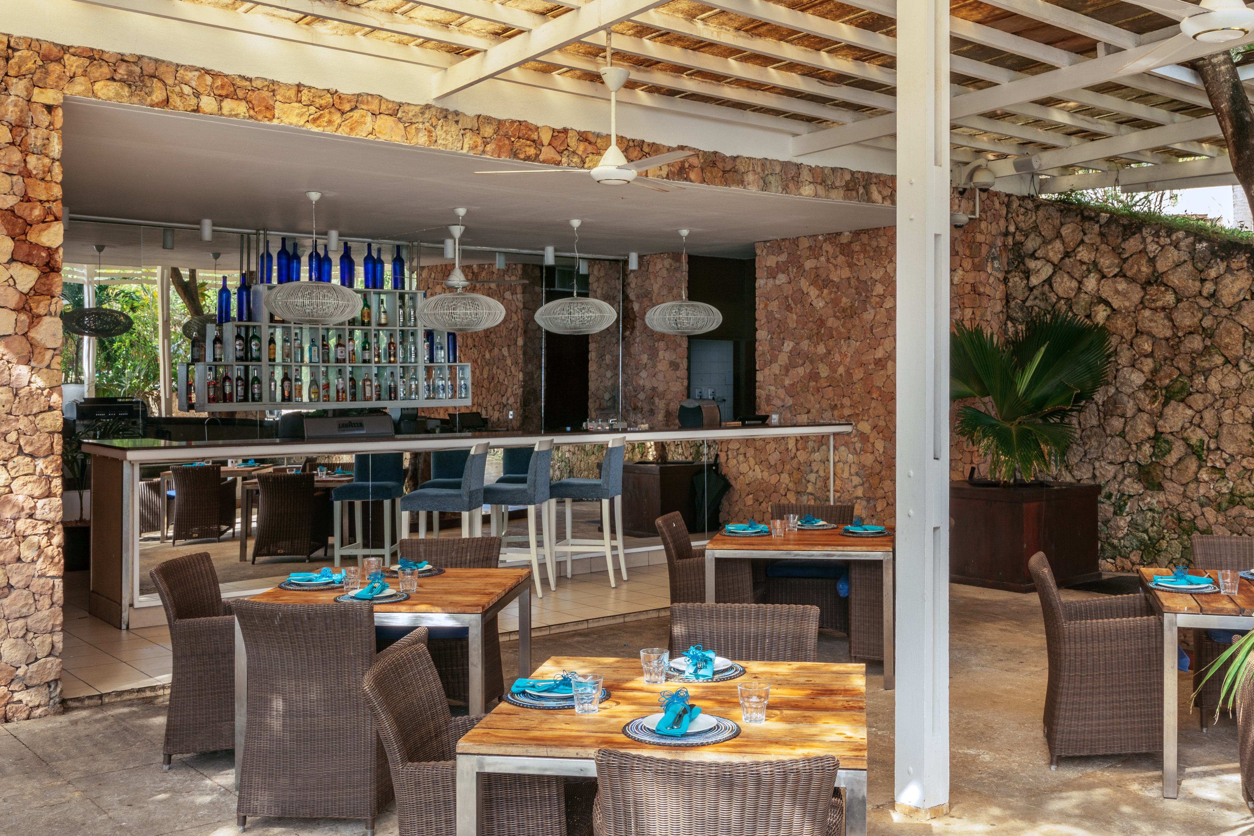Outdoor restaurant bar with stone walls, wooden tables, and blue accents.