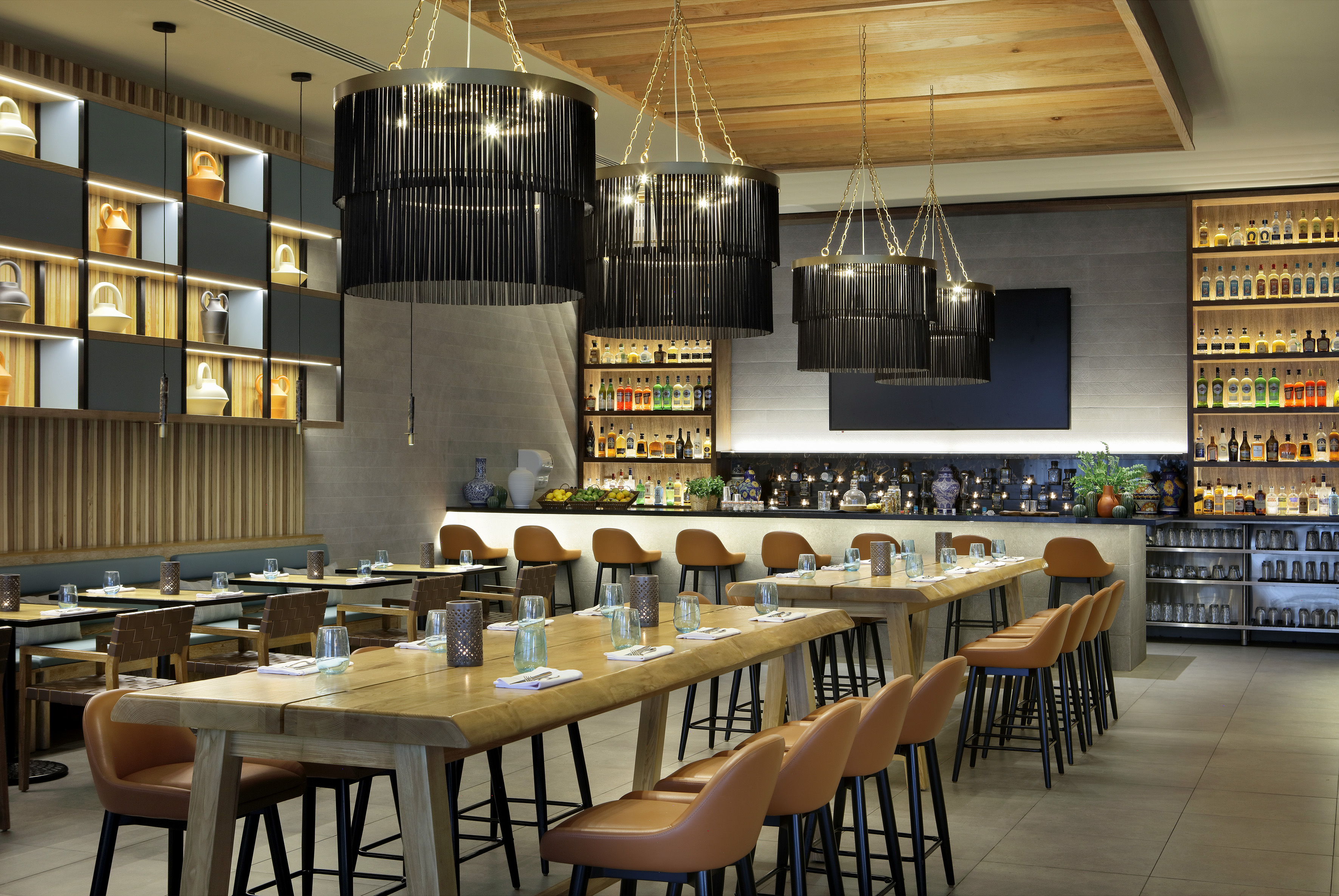 Modern restaurant interior with stylish bar, dining tables, and chandeliers.
