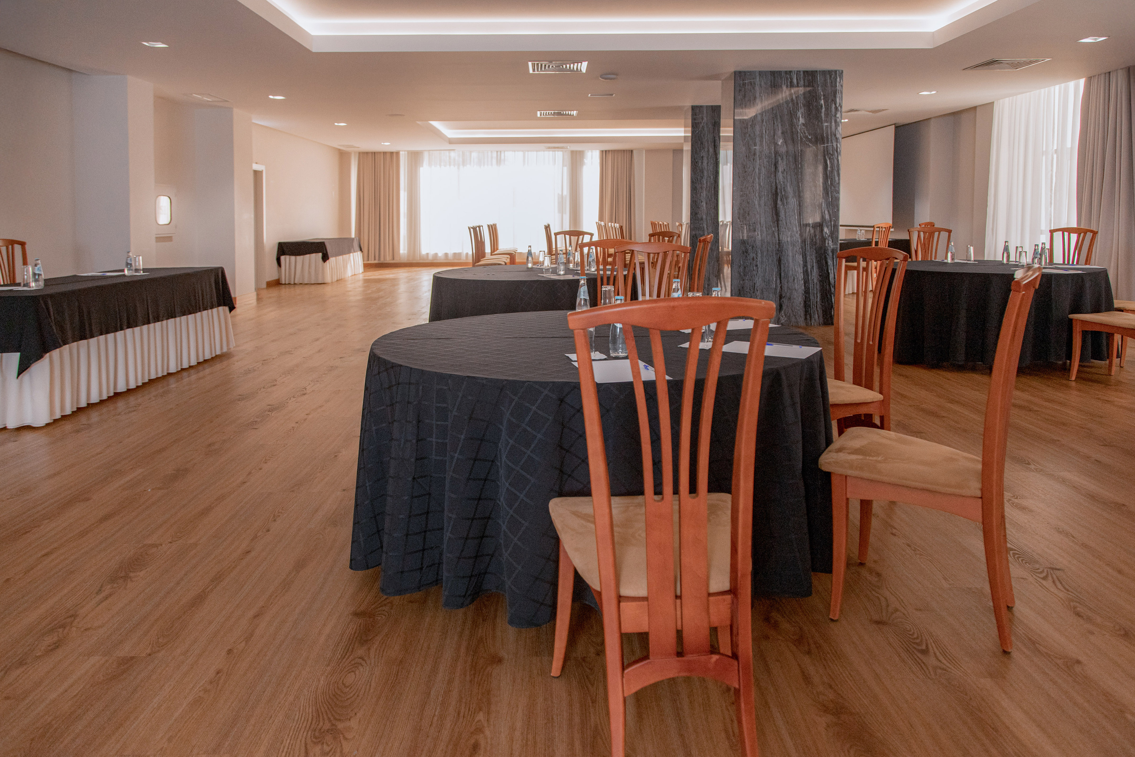Prepared conference room with round tables, dark linens, wood chairs, wood floor.