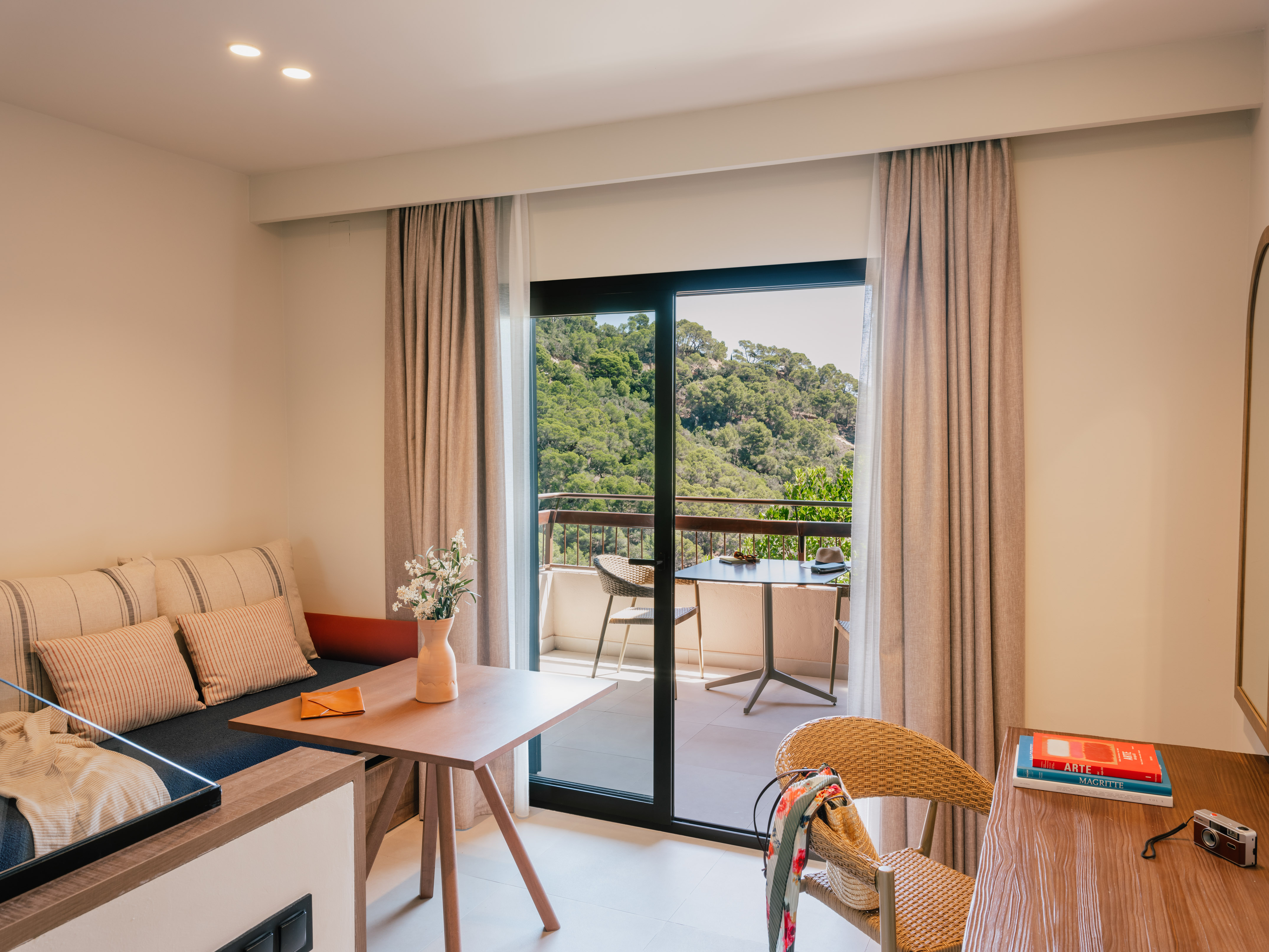 Modern hotel suite with balcony and lush green mountain forest view.