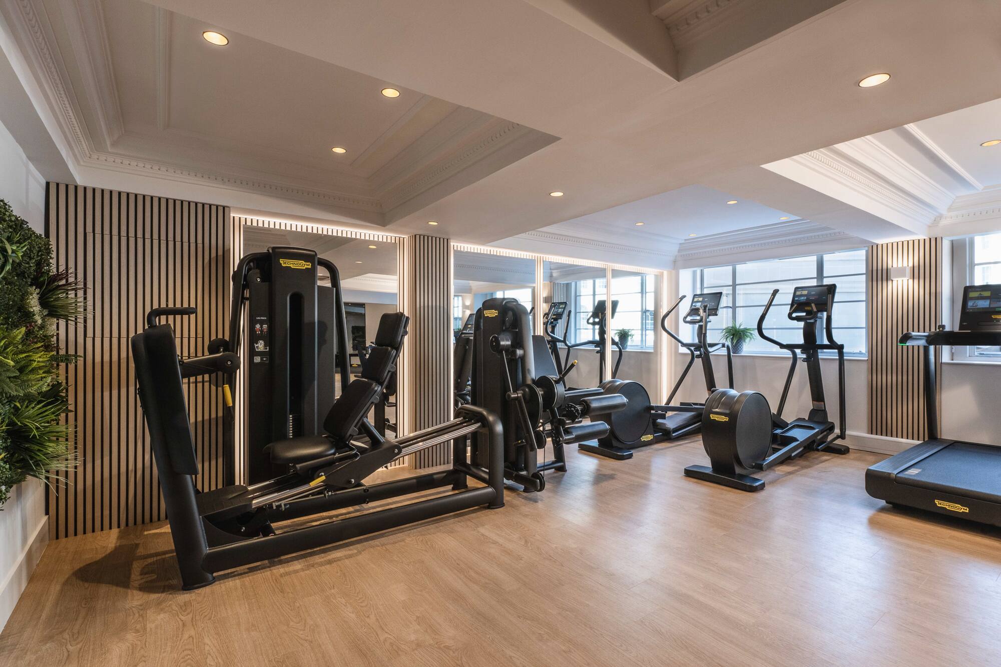 Bright, modern gym with Technogym cardio, strength equipment, and wood floor.