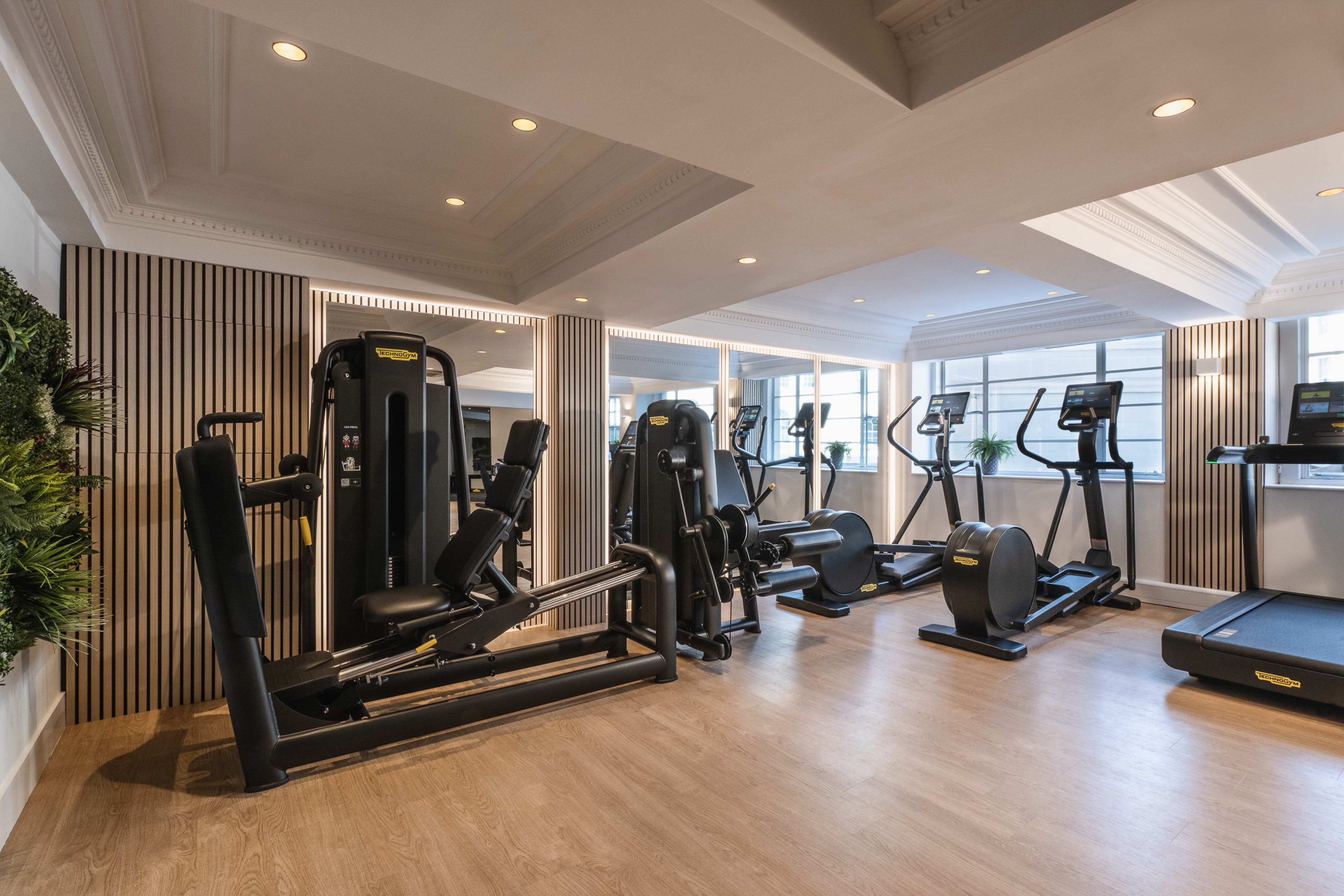 Bright, modern gym with Technogym cardio, strength equipment, and wood floor.
