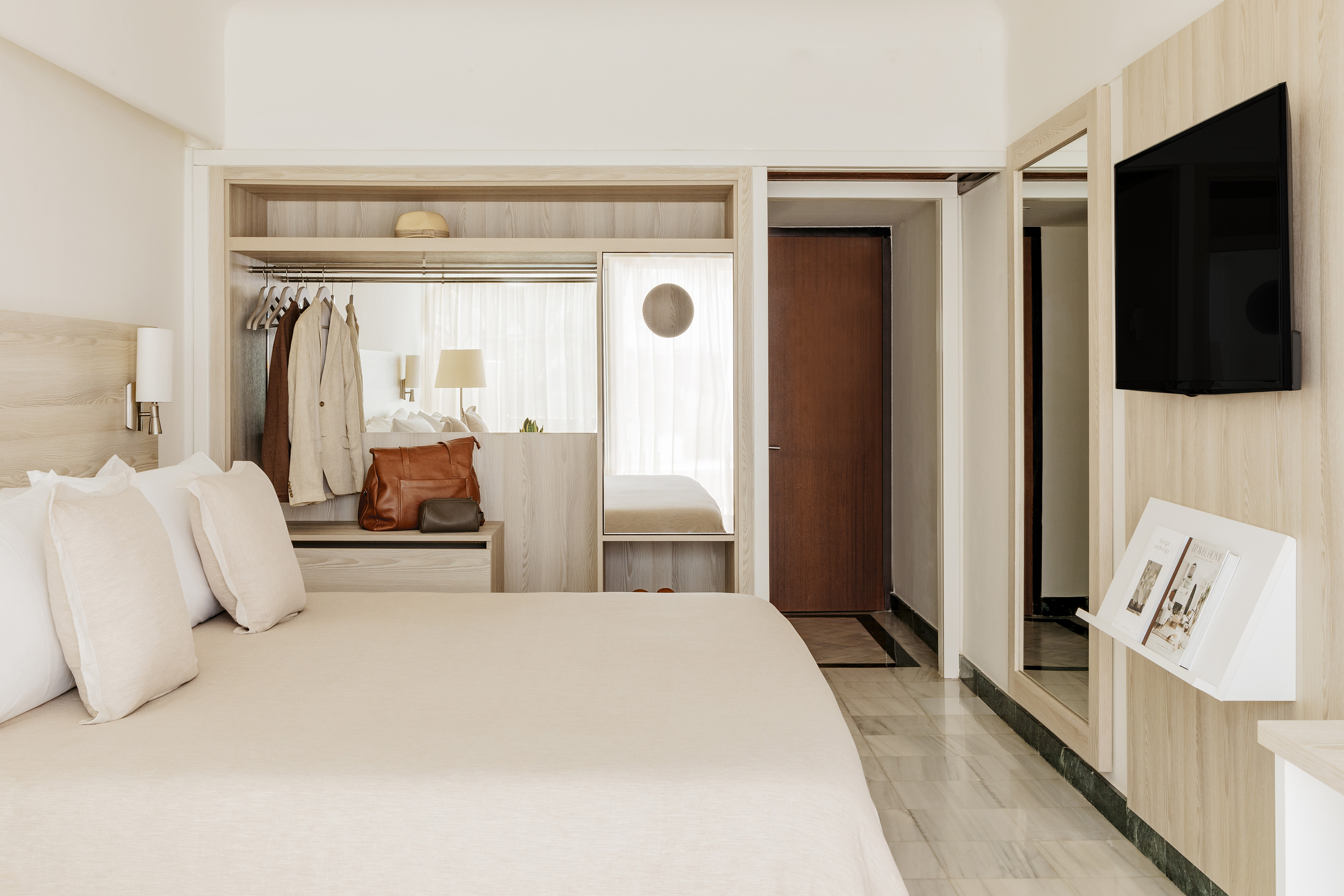 Modern hotel bedroom with neutral decor, built-in wardrobe, and mounted TV.