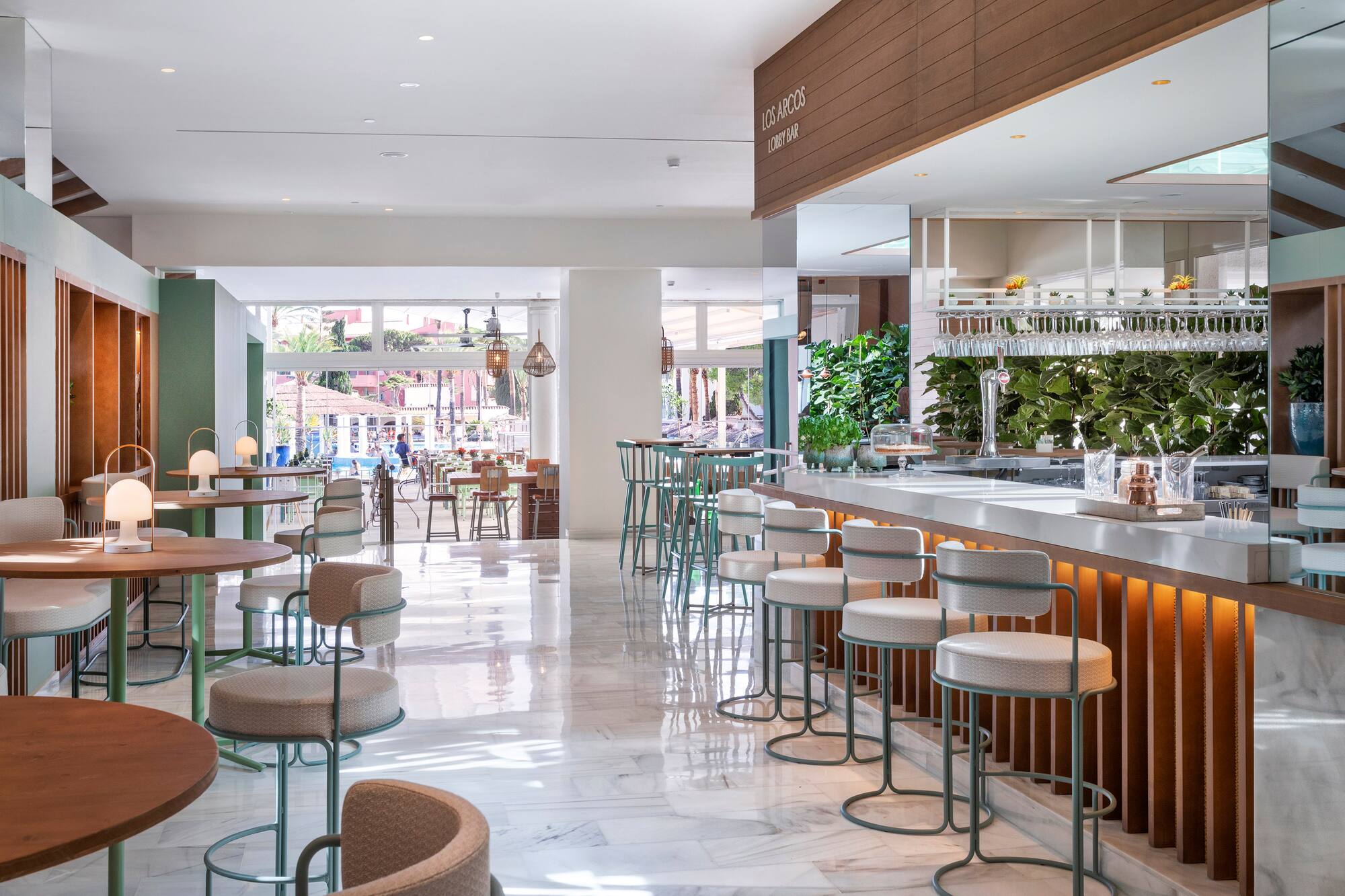 Bright Los Arcos lobby bar with modern design, marble floors, and lush plants.