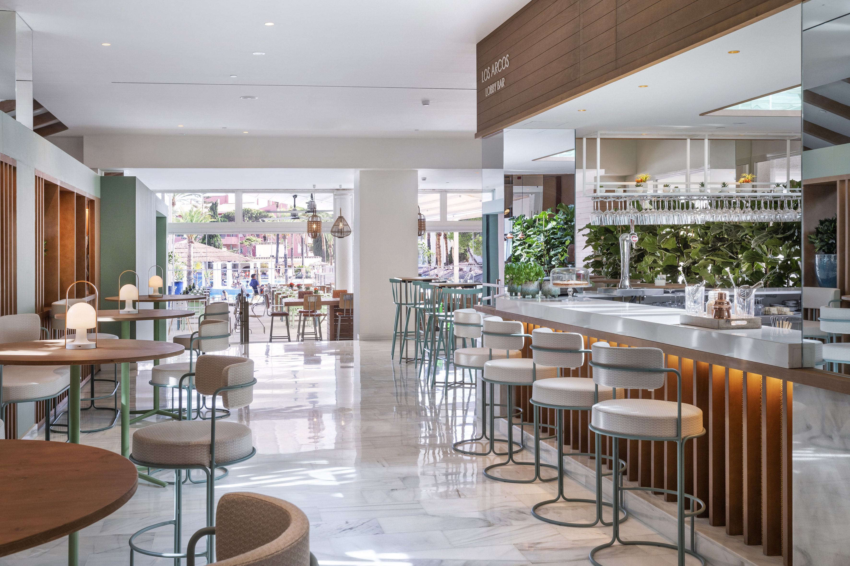 Bright Los Arcos lobby bar with modern design, marble floors, and lush plants.