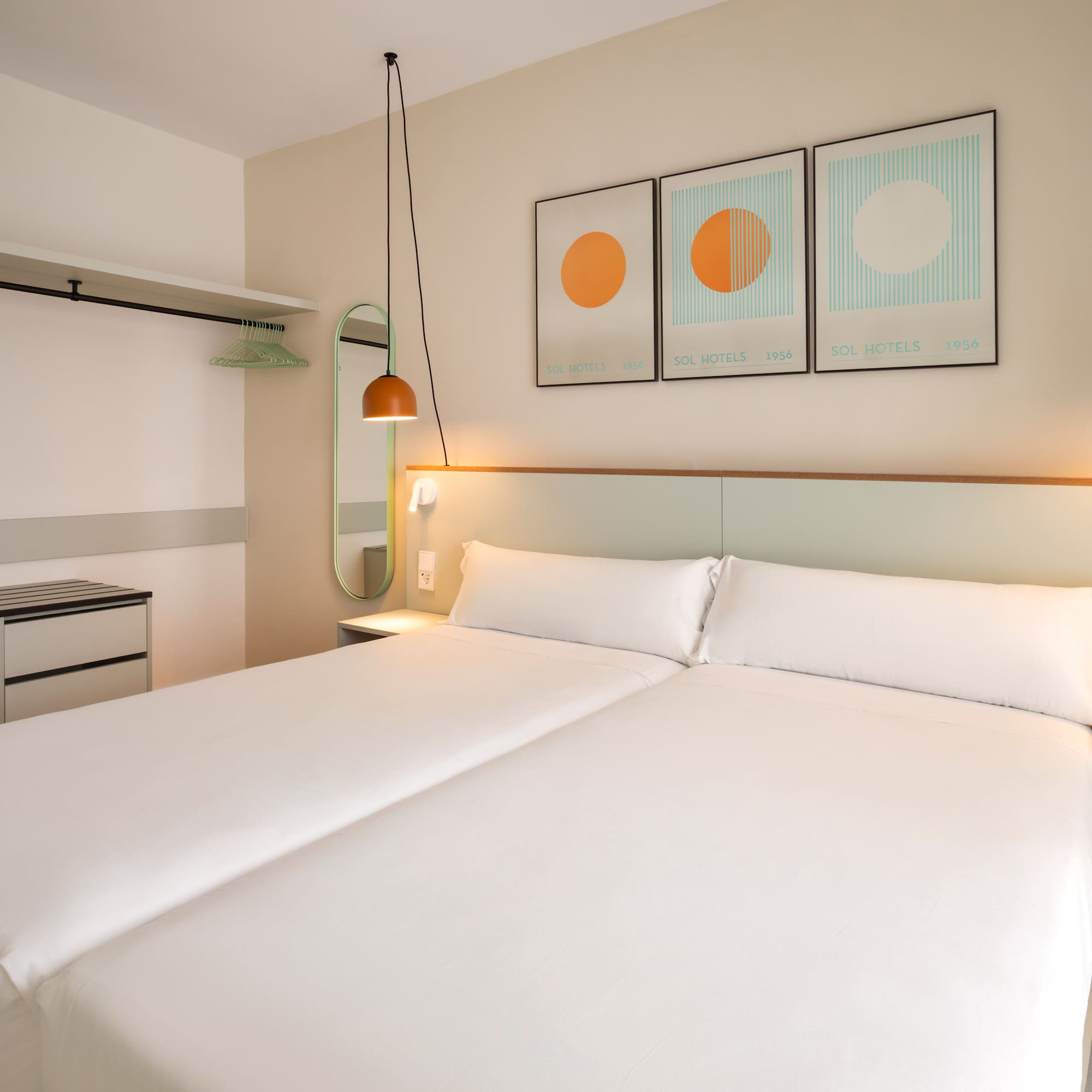 Hotel room with two beds, white bedding, orange hanging lamps, and open wardrobe.