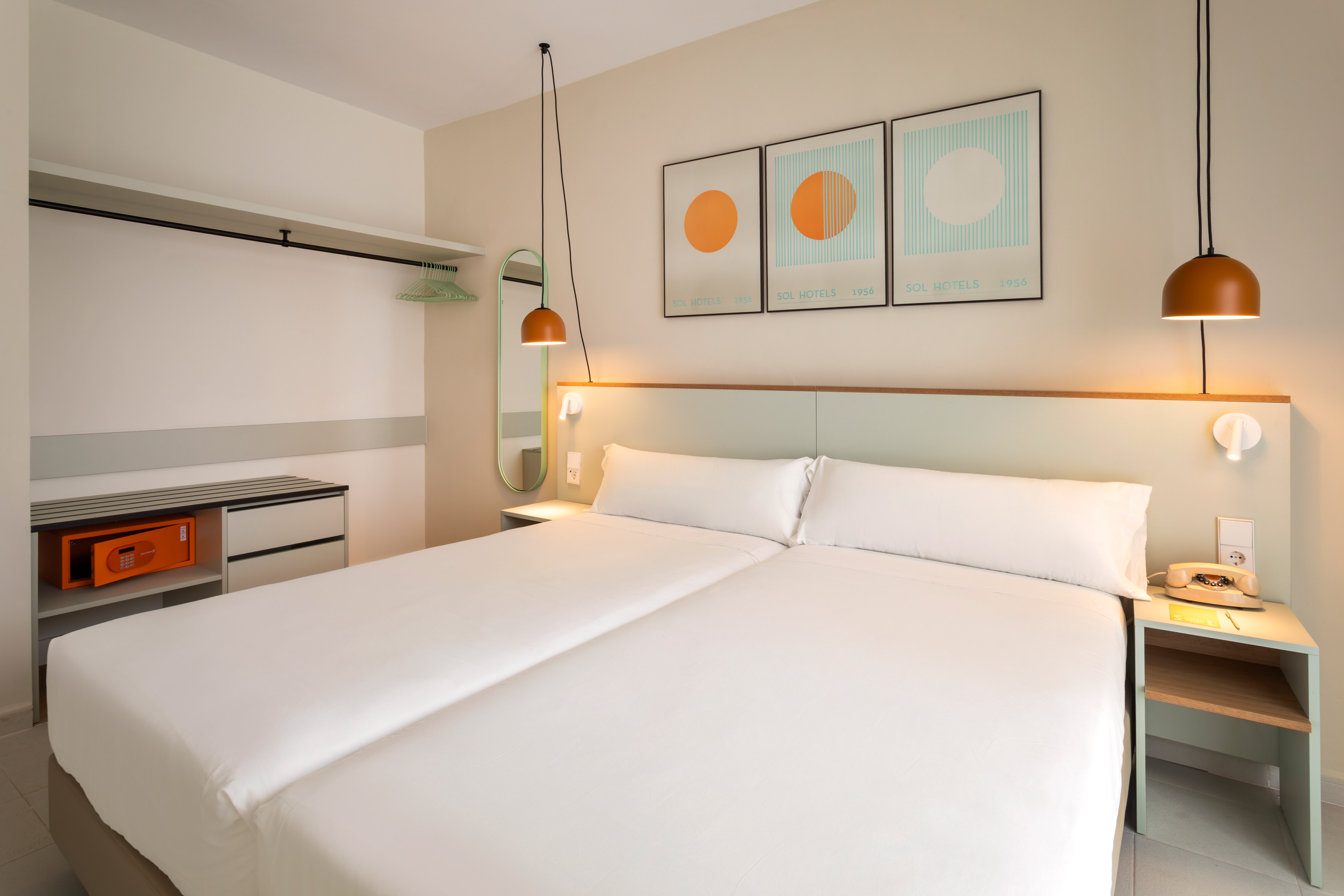 Modern hotel room with twin beds, minimalist decor, and wardrobe with safe.