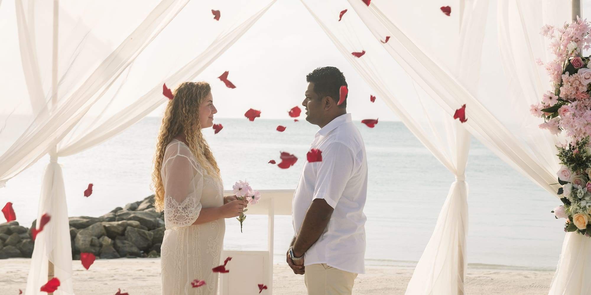 a man and woman standing under a canopy with flowers falling from the ground