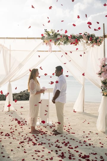 a man and woman standing under a canopy with flowers falling from the ground