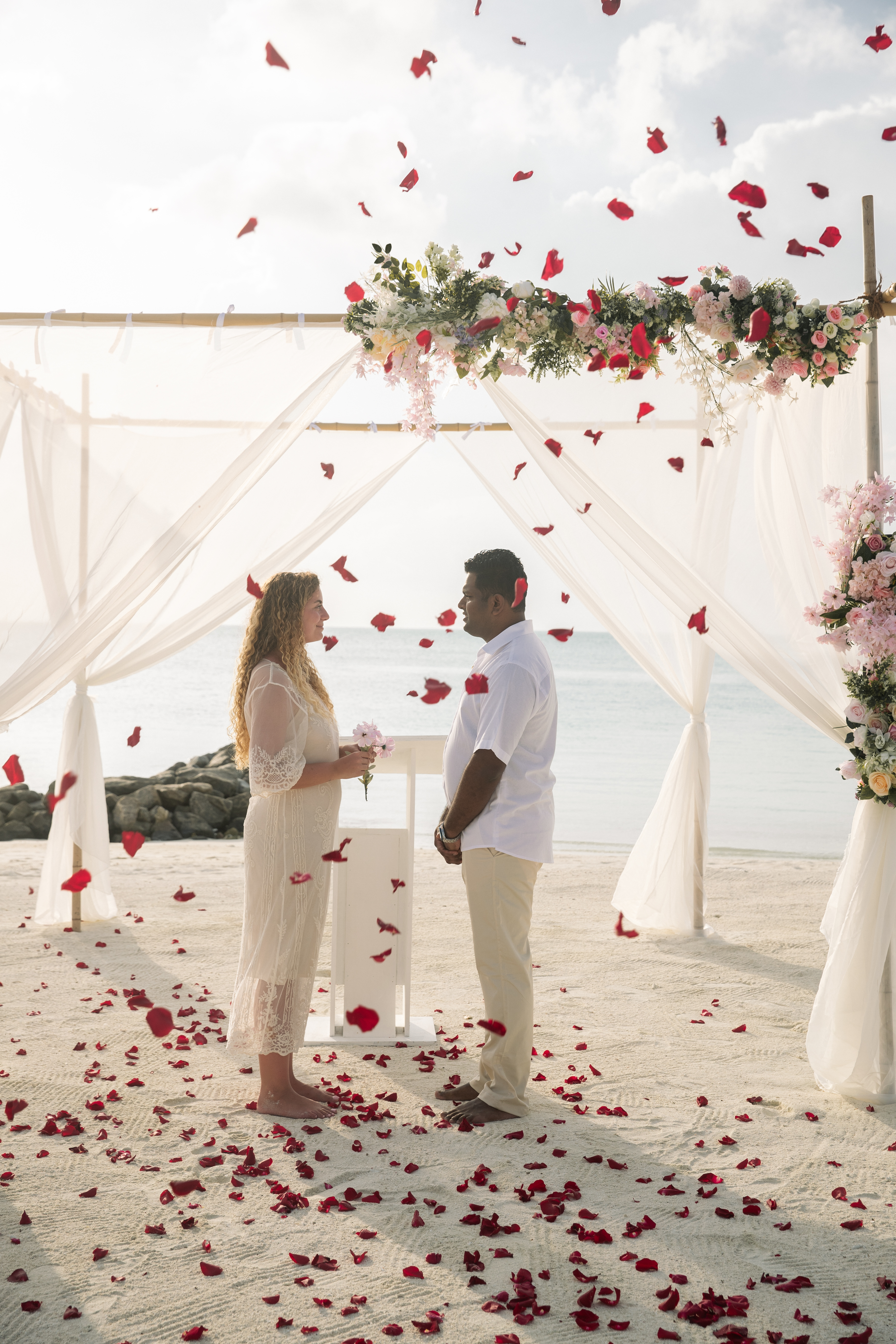 a man and woman standing under a canopy with flowers falling from the ground