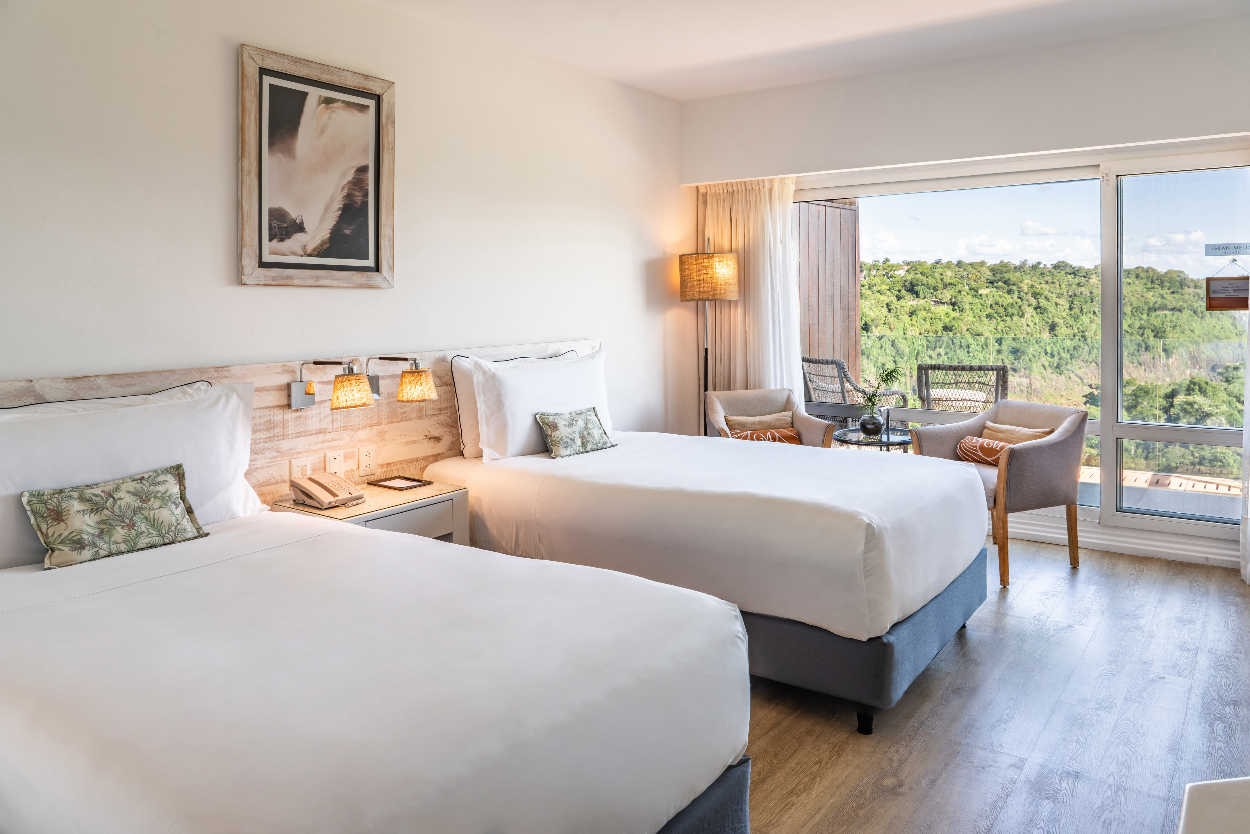 Twin hotel room with forest view balcony, waterfall art, and modern decor.