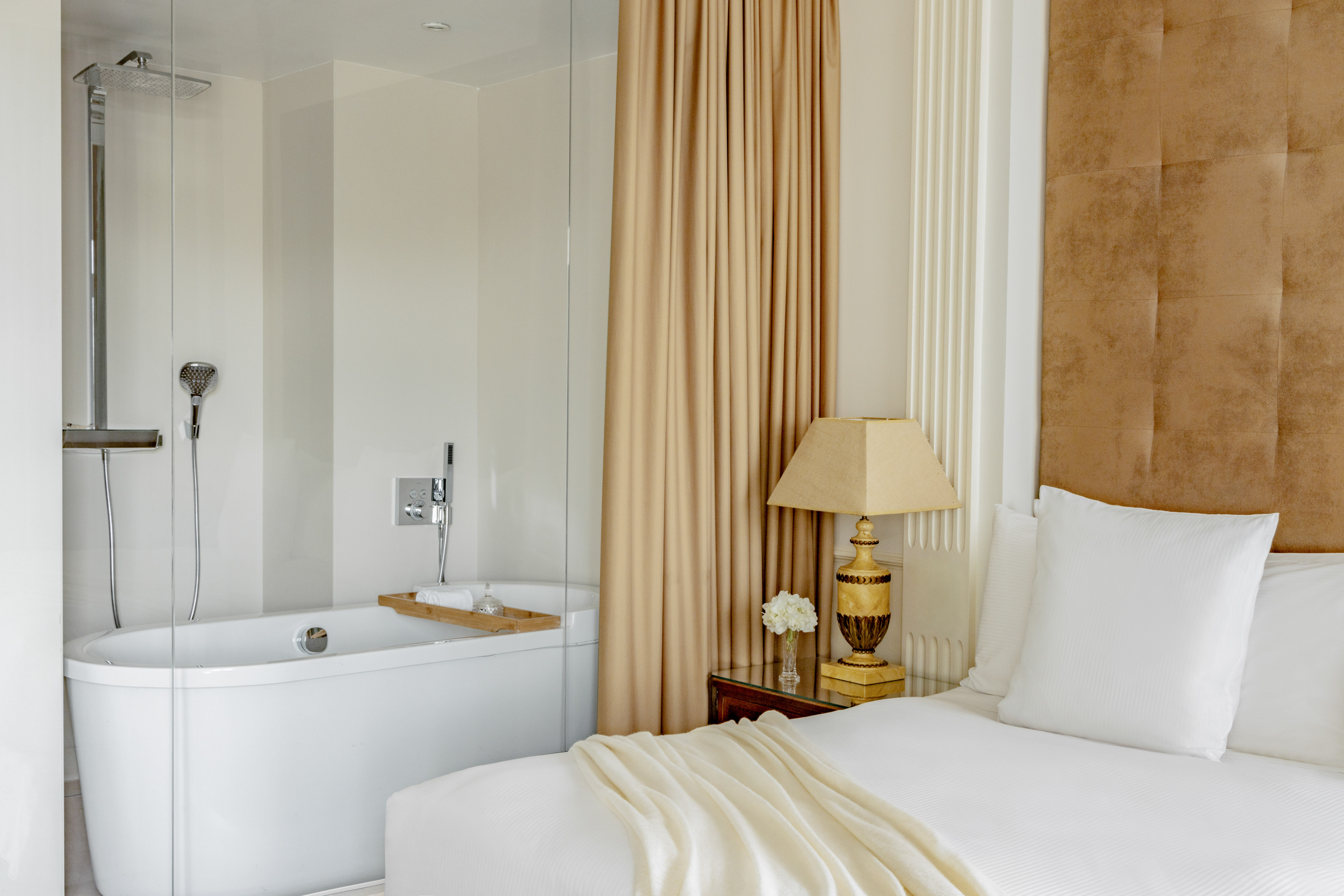 Modern hotel bedroom with freestanding tub, glass shower, and chic decor.