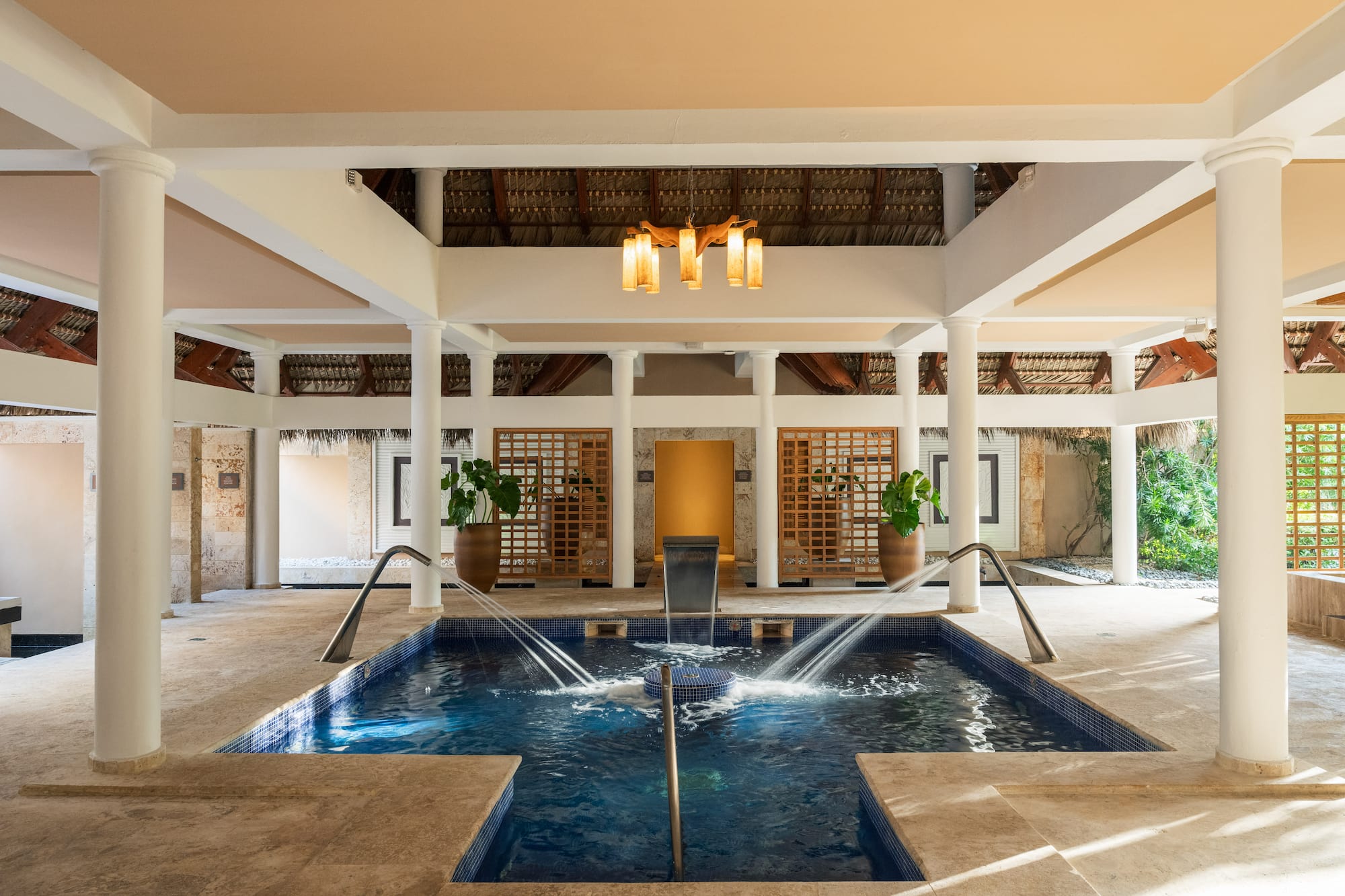 Piscina de hidromasaje en spa de lujo con pilares y techo de palma, estilo tropical.