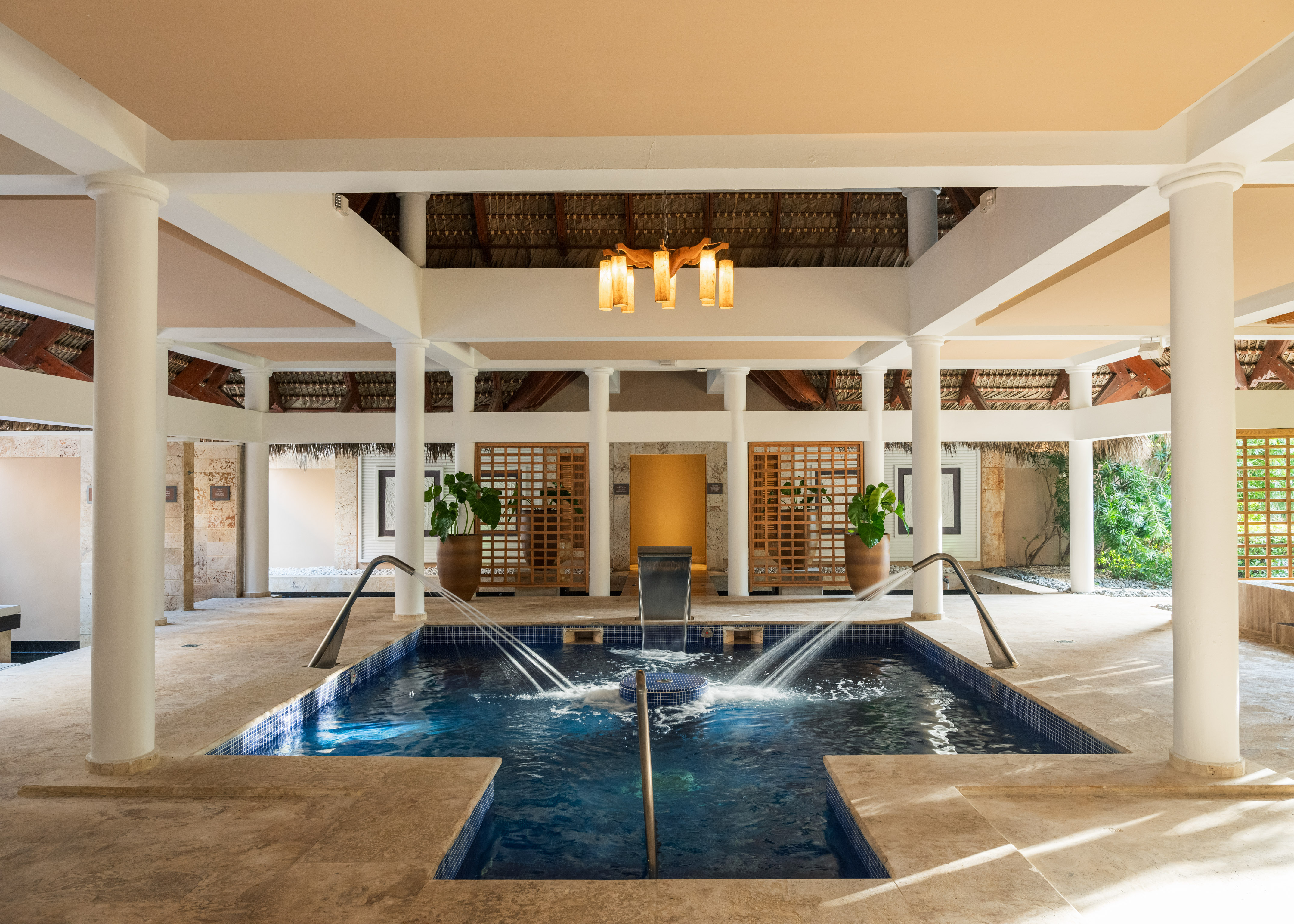 Piscina de hidromasaje en spa de lujo con pilares y techo de palma, estilo tropical.