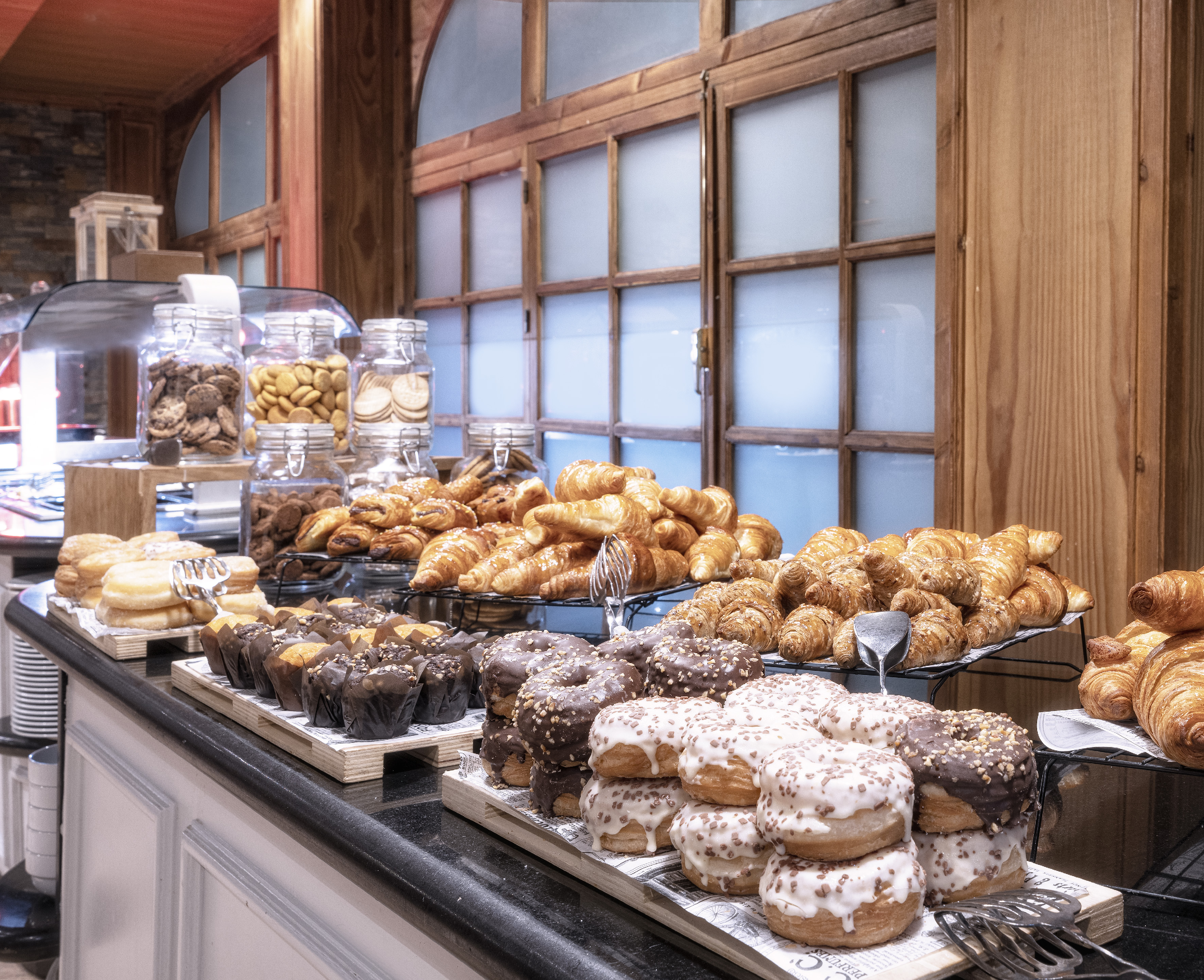 Breakfast buffet spread with croissants, glazed and chocolate donuts, muffins, cookies.