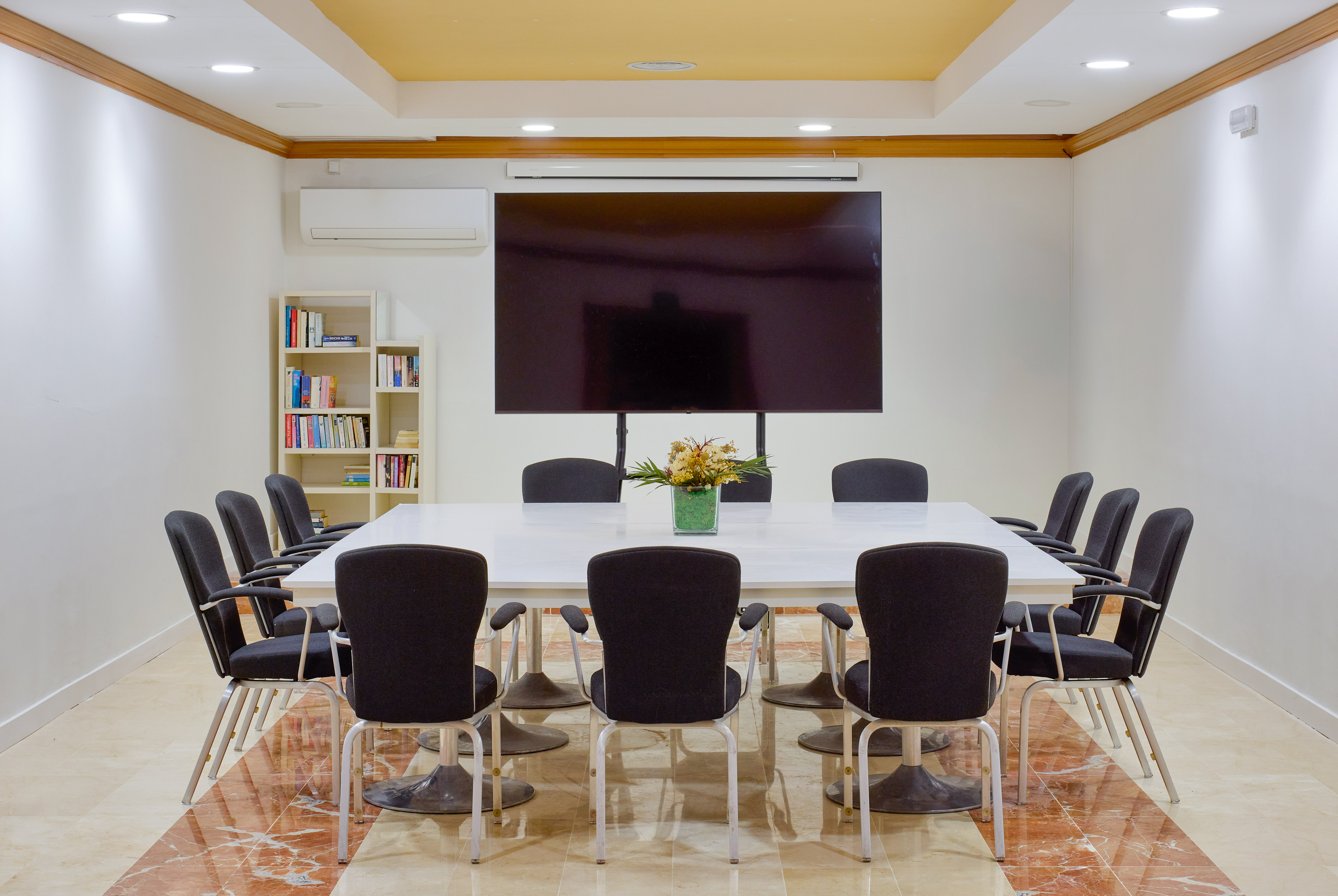 Modern corporate meeting room with large screen, white table, and grey chairs.
