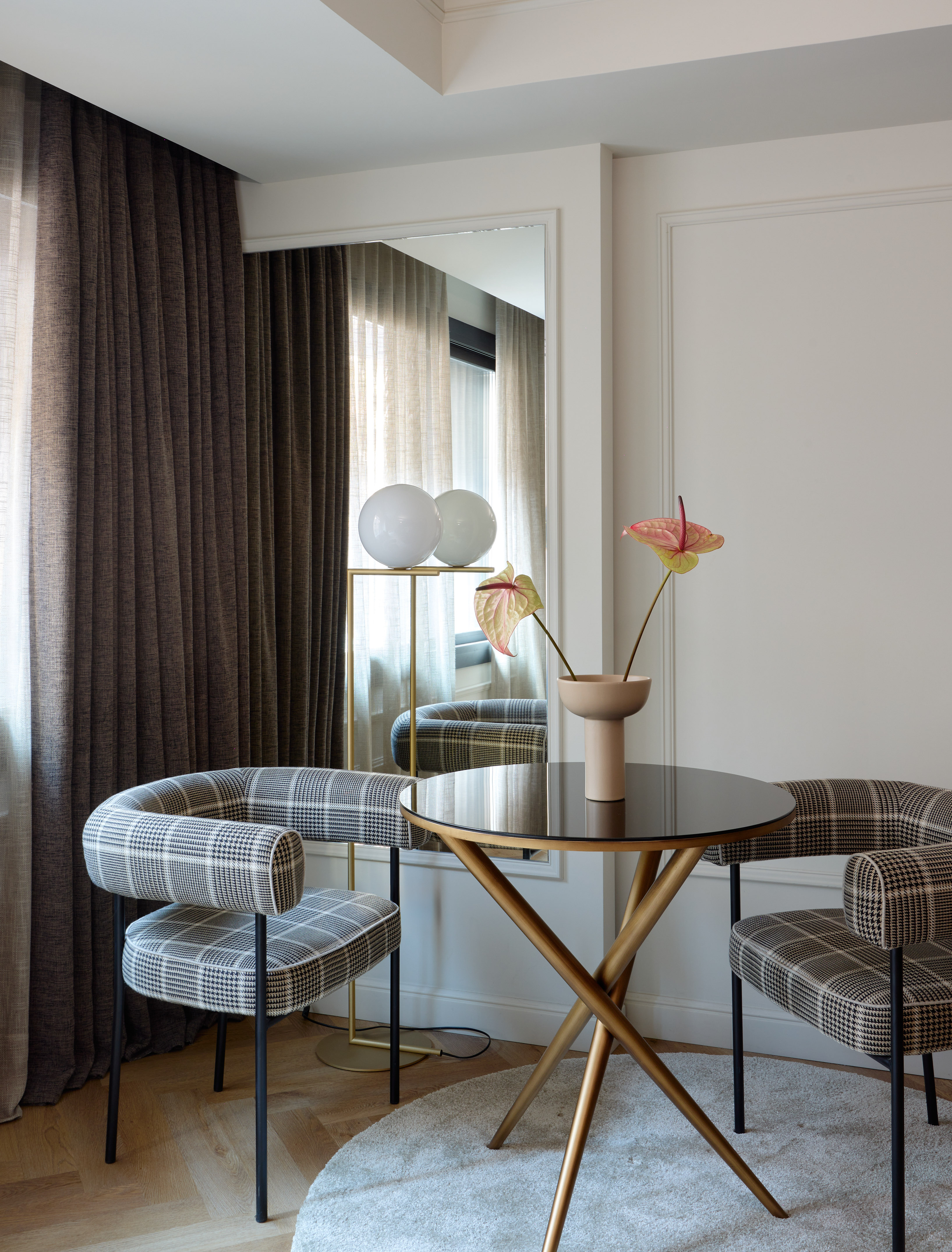 Modern dining area with plaid armchairs, gold table, and anthurium flowers.