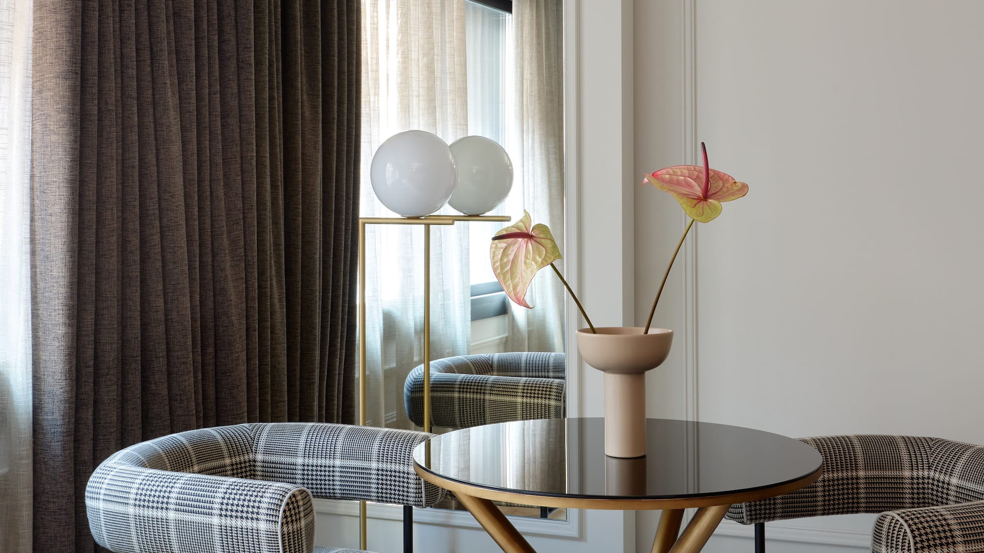 Modern dining area with plaid armchairs, gold table, and anthurium flowers.