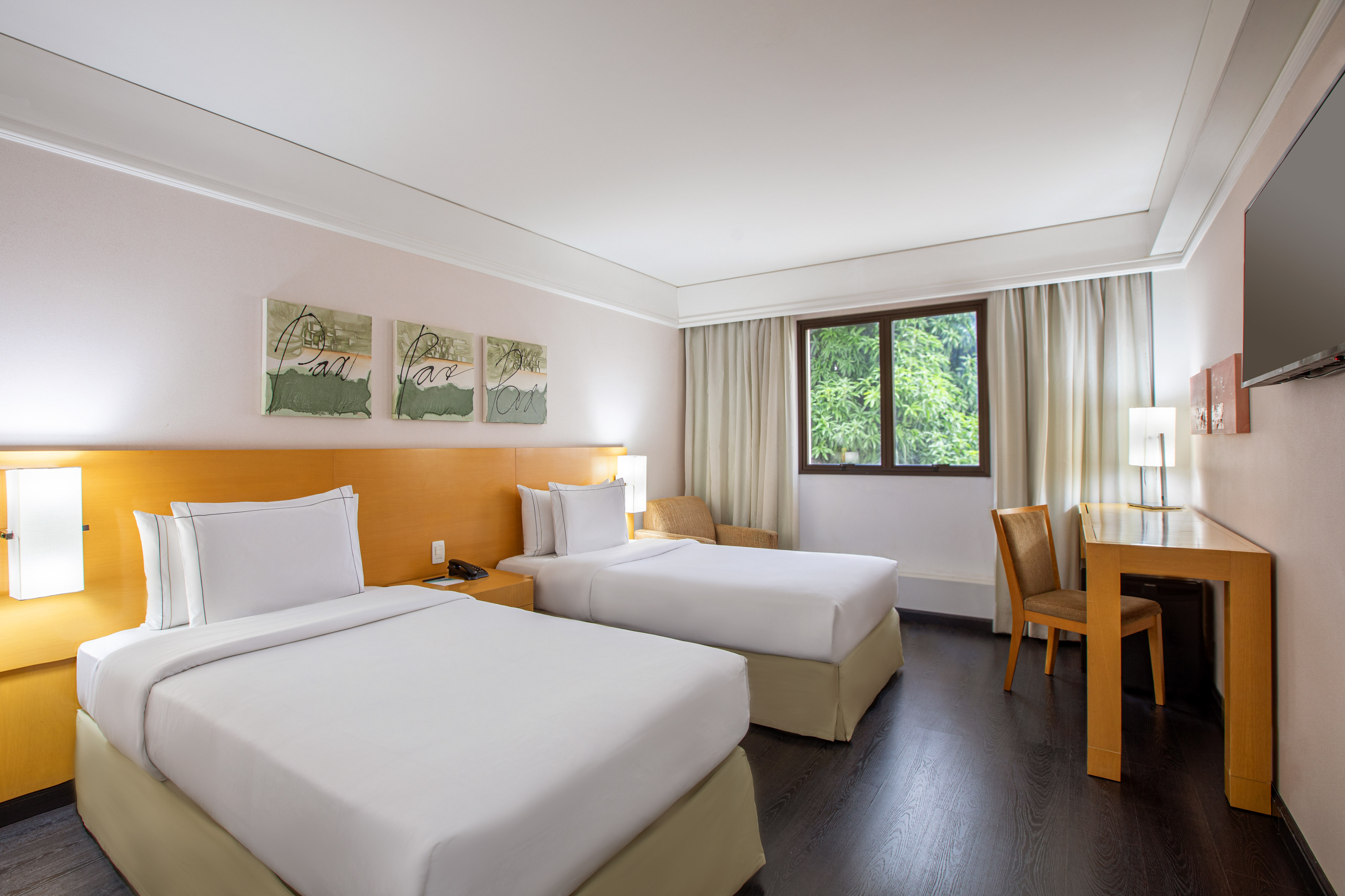 Hotel room with two twin beds, hardwood floor, window, and work desk.